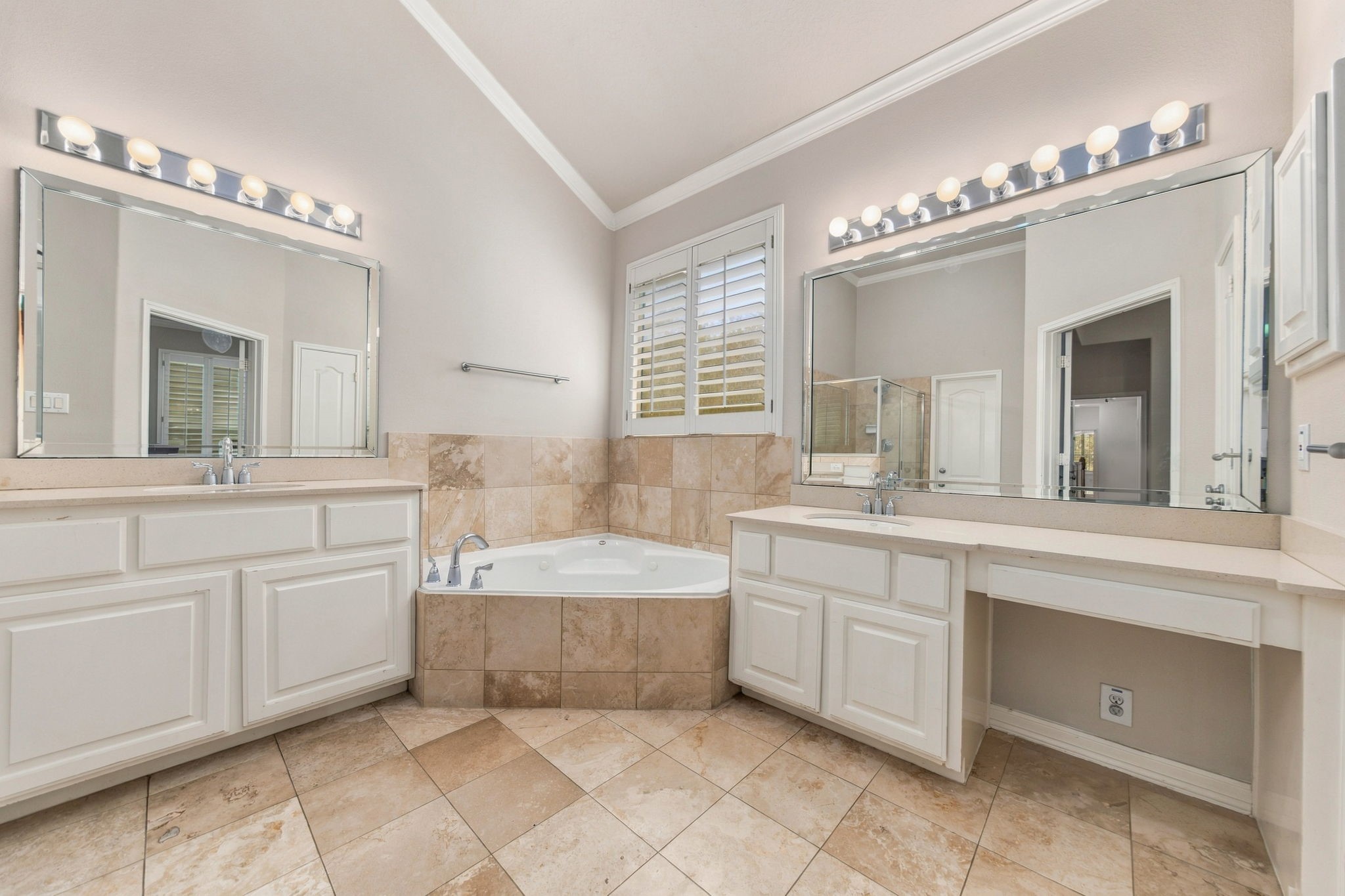 The primary bath offers separate vanities, a jetted soaking tub, tile flooring & a dedicated seated vanity area.