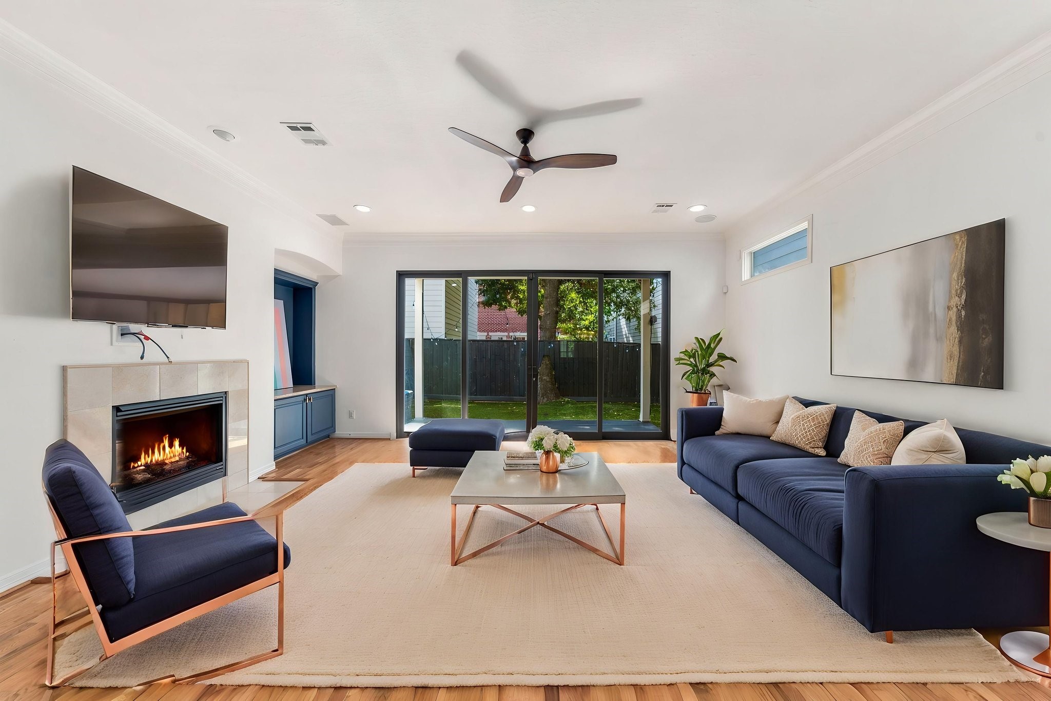 A spacious, light-filled living room featuring hardwood floors, fireplace, crown molding & built-in surround sound. Expansive sliding glass doors overlook the private backyard, creating a seamless connection between indoor & outdoor living. Virtually staged.