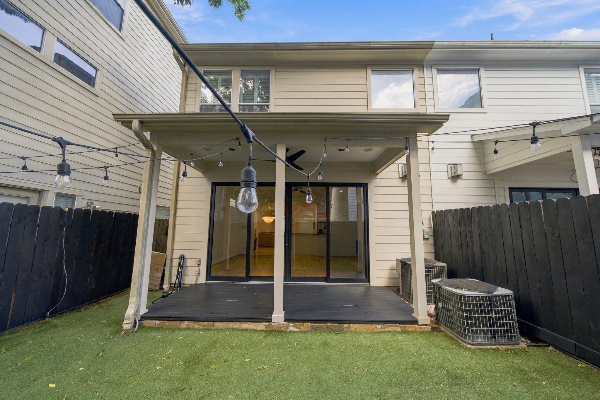 A covered patio extends the living space outdoors, with sliding glass doors connecting directly to the main living area. String lighting adds a charming touch for evenings outside.