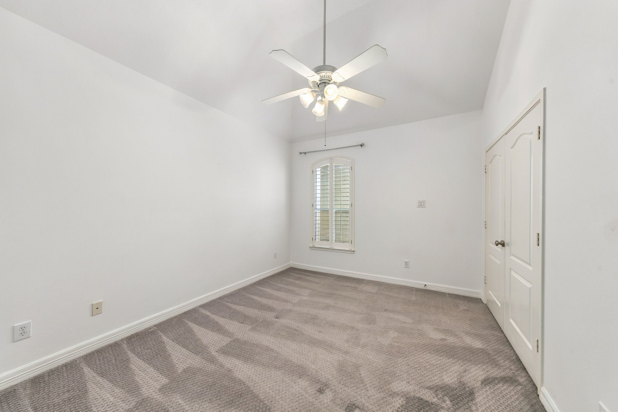 Unstaged view of the third secondary bedroom, highlighting its vaulted ceiling, plantation shutters & closet.