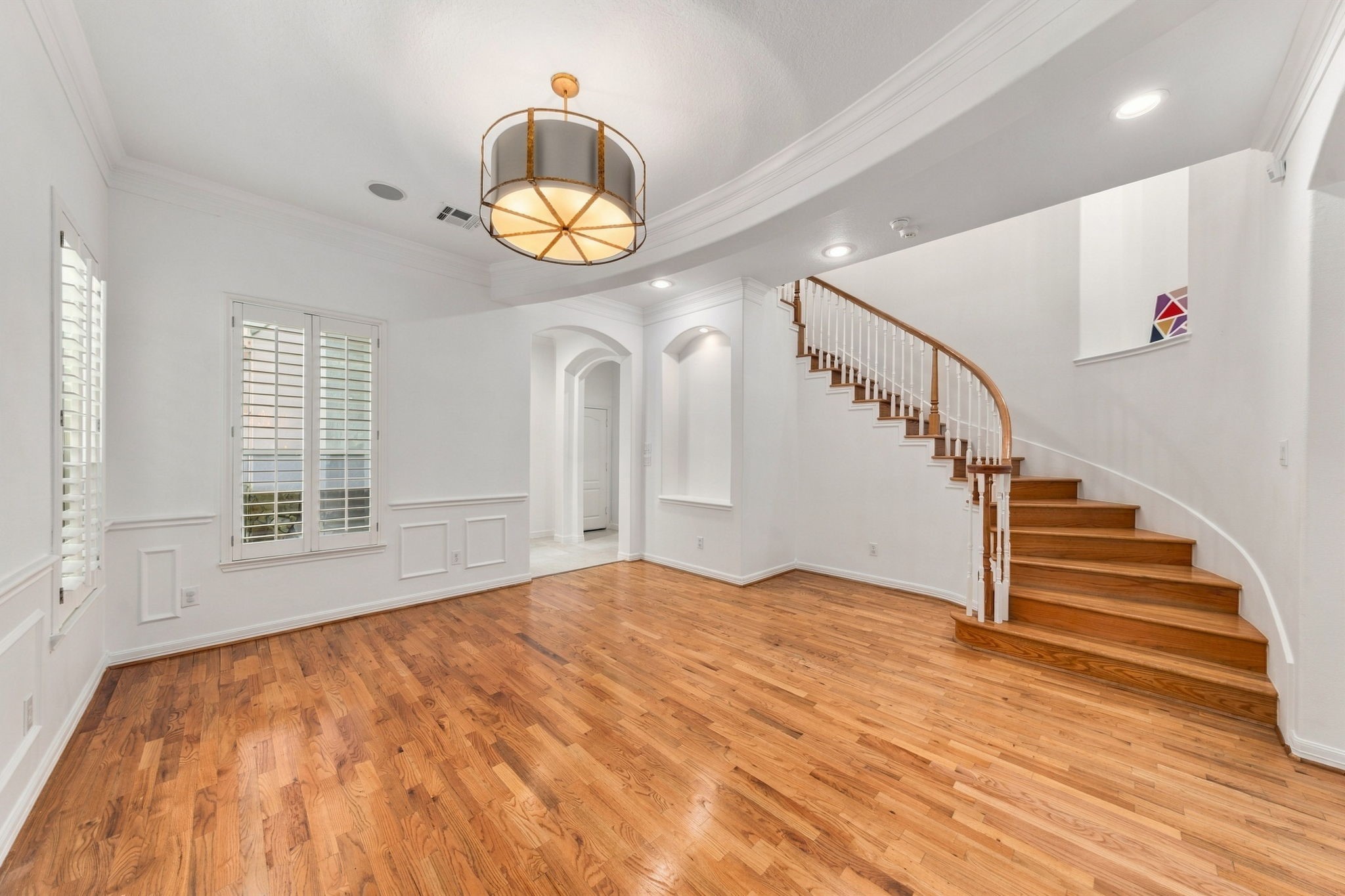 A lovely view of the curved staircase, rich hardwood floors & architectural archways that bring character to the main level.