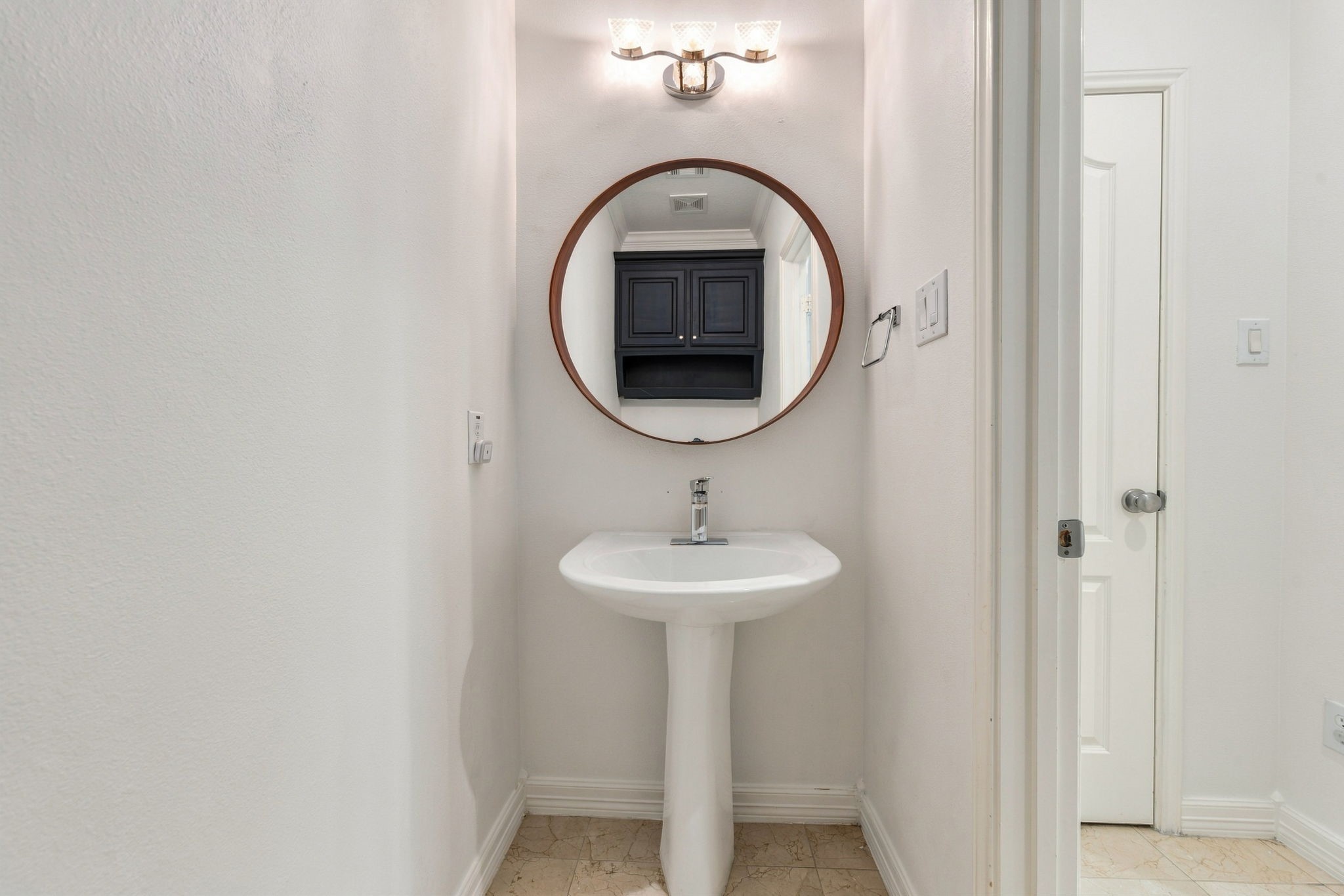 First-floor powder bath with a pedestal sink, contemporary fixtures & stylish round mirror.