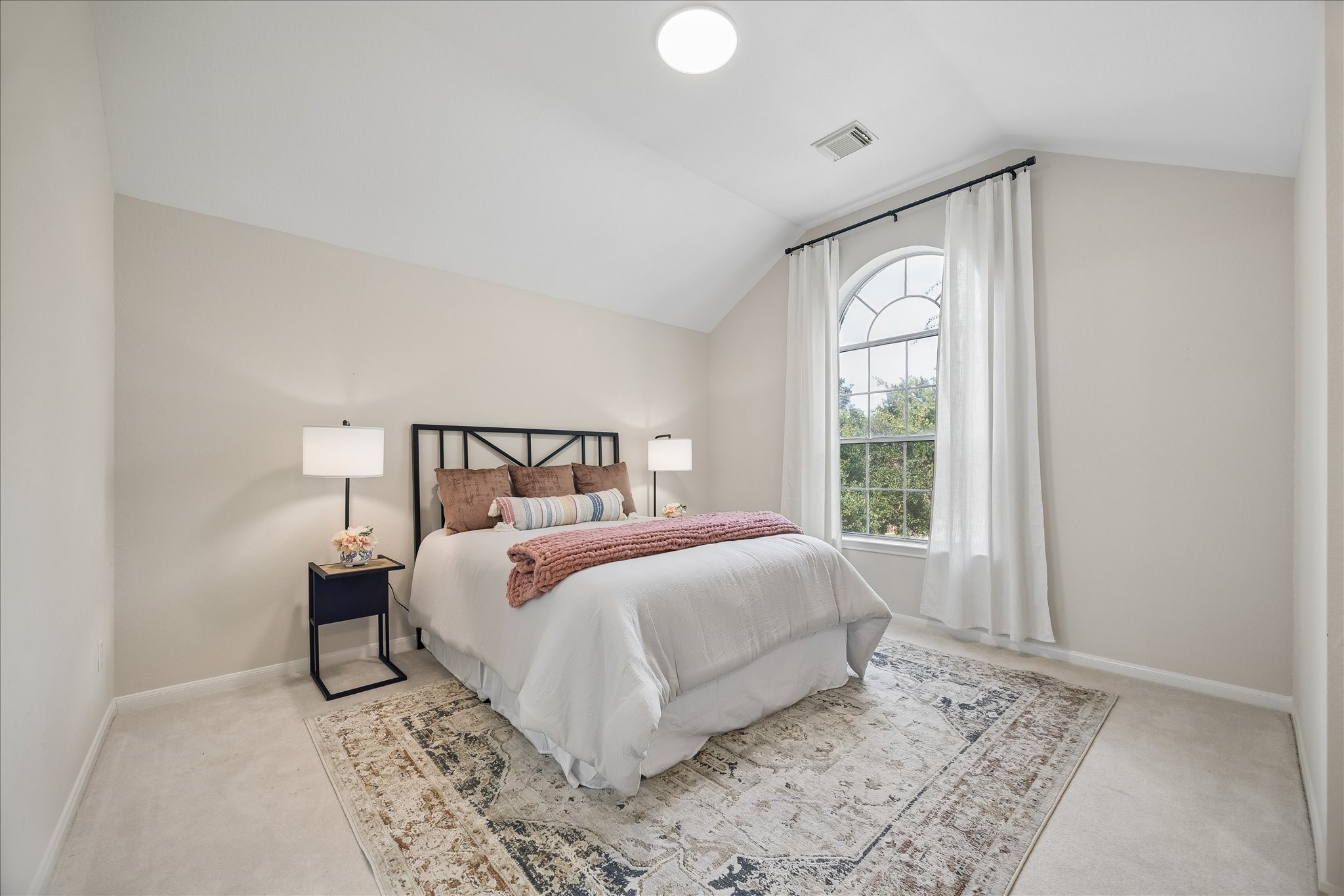 This spacious secondary bedroom #2 features soaring ceilings, abundant natural light, and a large arched window that creates a bright and comfortable retreat.
