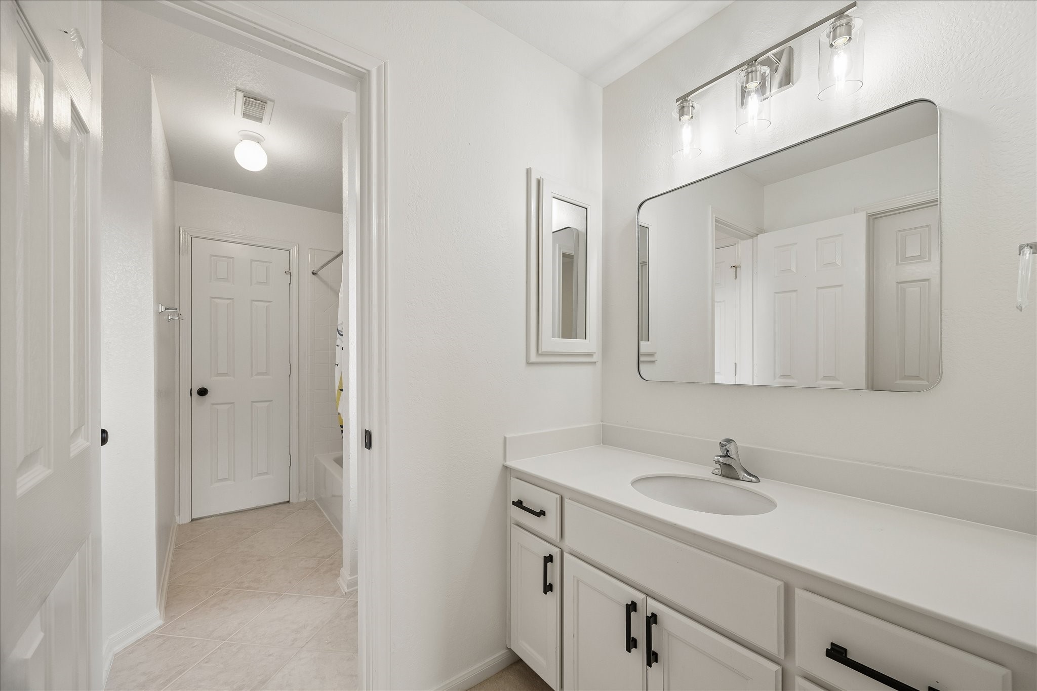 Bright lighting and updated finishes create a fresh, inviting atmosphere throughout the bath. Easy access to the adjoining shower and dressing areas adds to the home's thoughtful design.