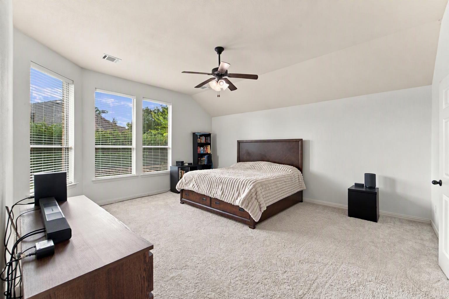 This generously sized primary bedroom is a comfortable place to start and end your day. Soft carpet, a ceiling fan, and a wall of windows bring in plenty of natural light. Edited using AI tools.