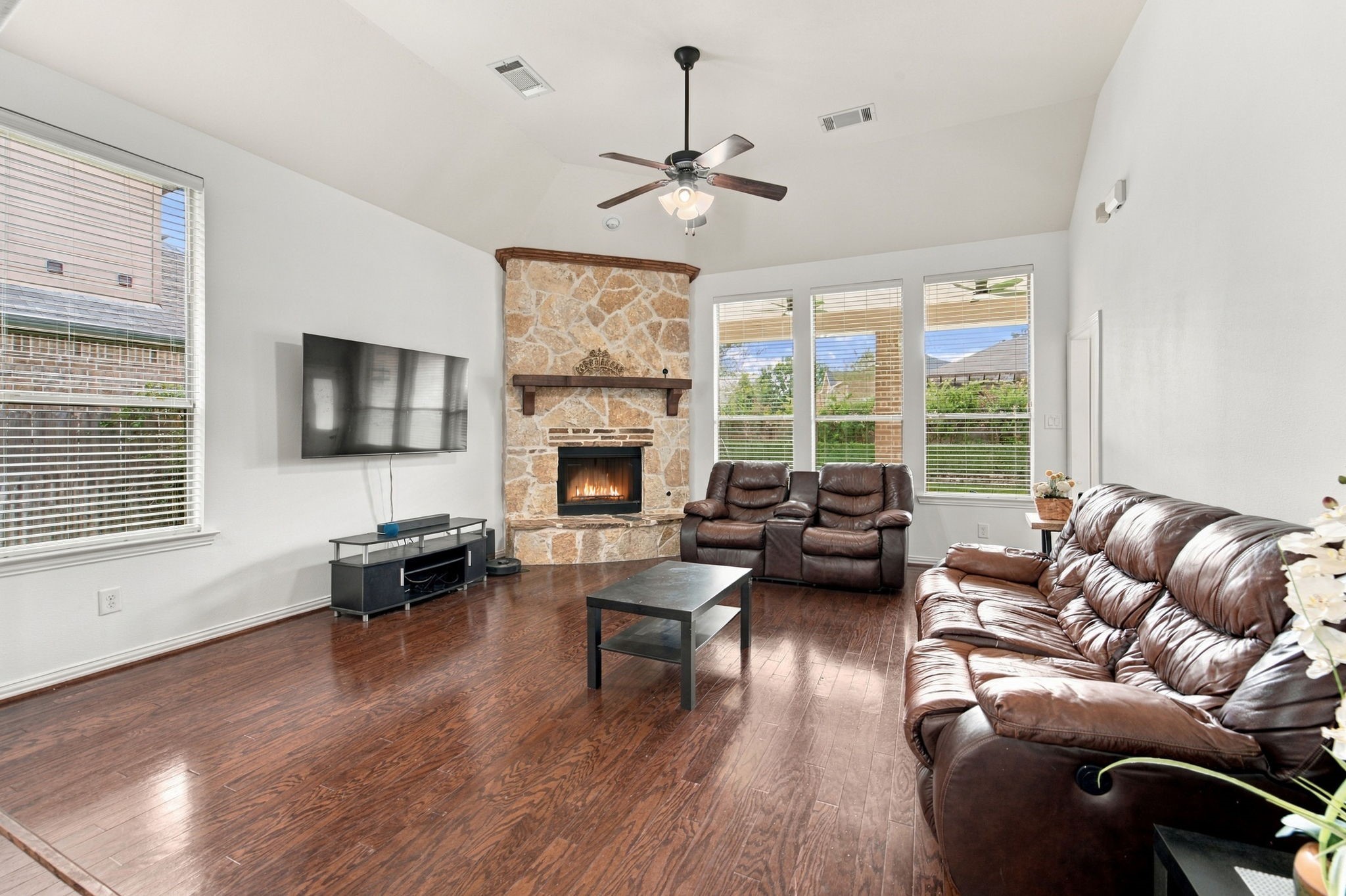 Vaulted ceilings give this generously sized living room an open, airy feel. The stone gas fireplace sets a cozy tone, and the windows bring in plenty of daylight, with easy access to the backyard through the back door.
