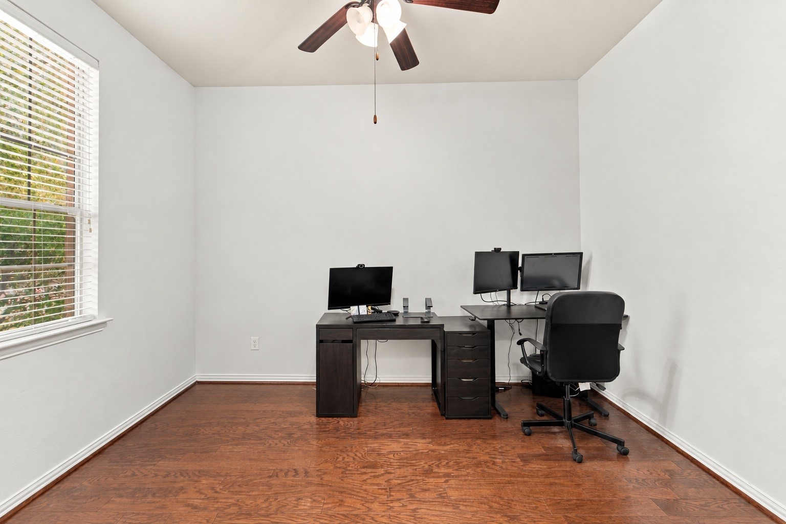 A dedicated home office makes working from home easy. Wood floors, a ceiling fan, and a large window bring in natural light, and theres plenty of room for a desk and workstation. Edited using AI tools.