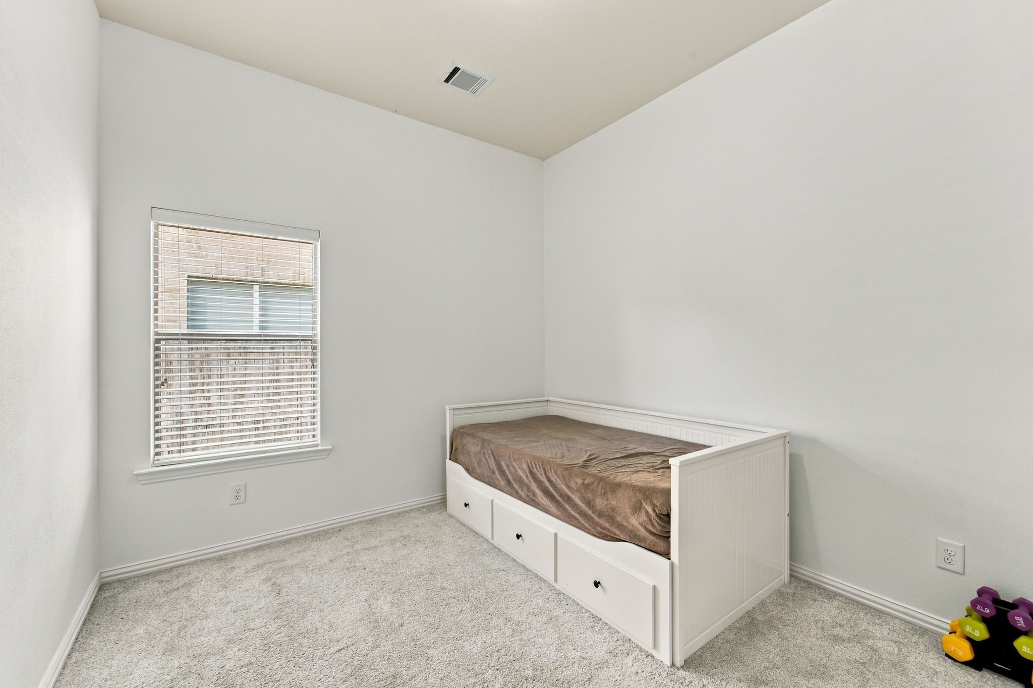 A comfortable secondary bedroom with soft carpet and a bright window, ready for guests, kids, or a hobby space.