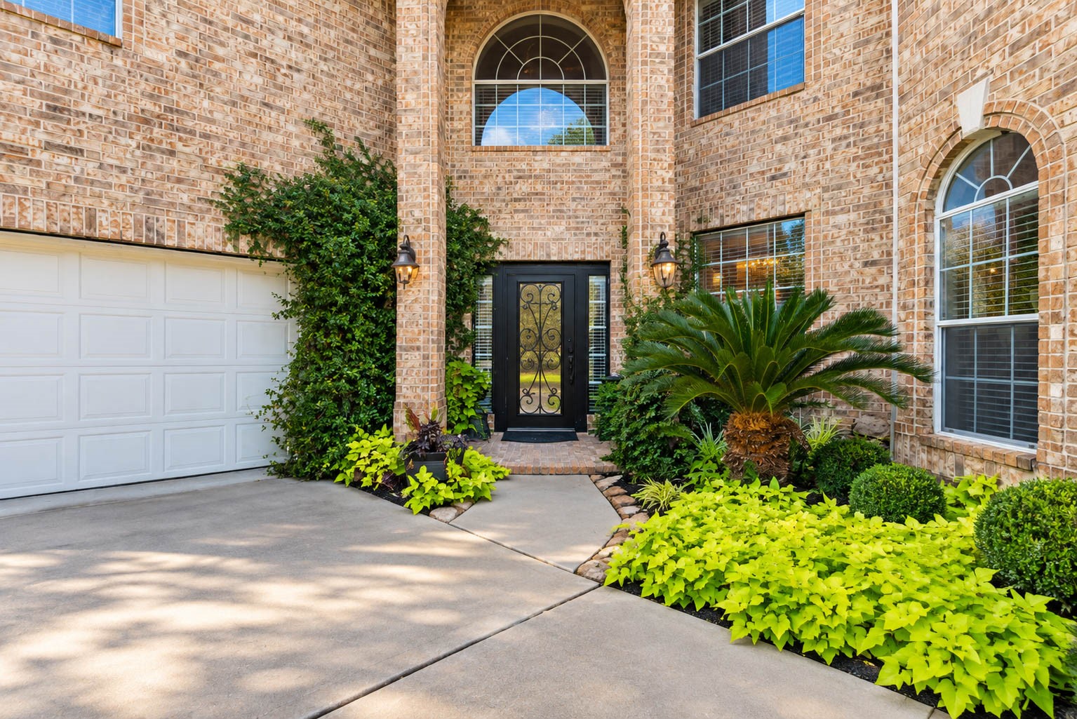A dramatic two-story recessed entry, framed by lush landscaping and an ornate iron-and-glass door, offers a glimpse of the elegance within.