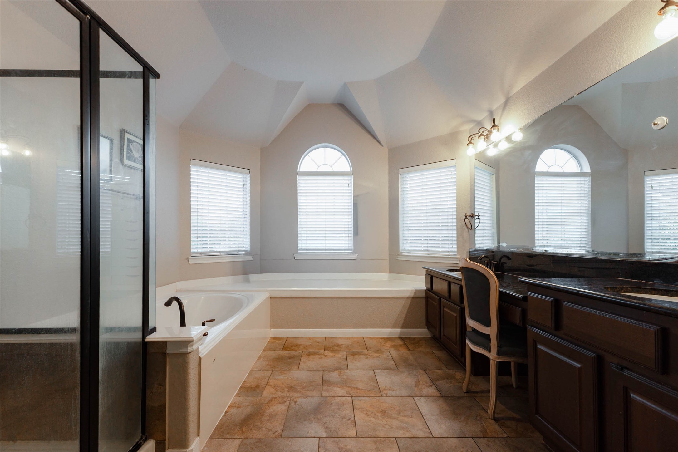 Vaulted ceiling details & an arched window create a relaxing primary en suite bath.