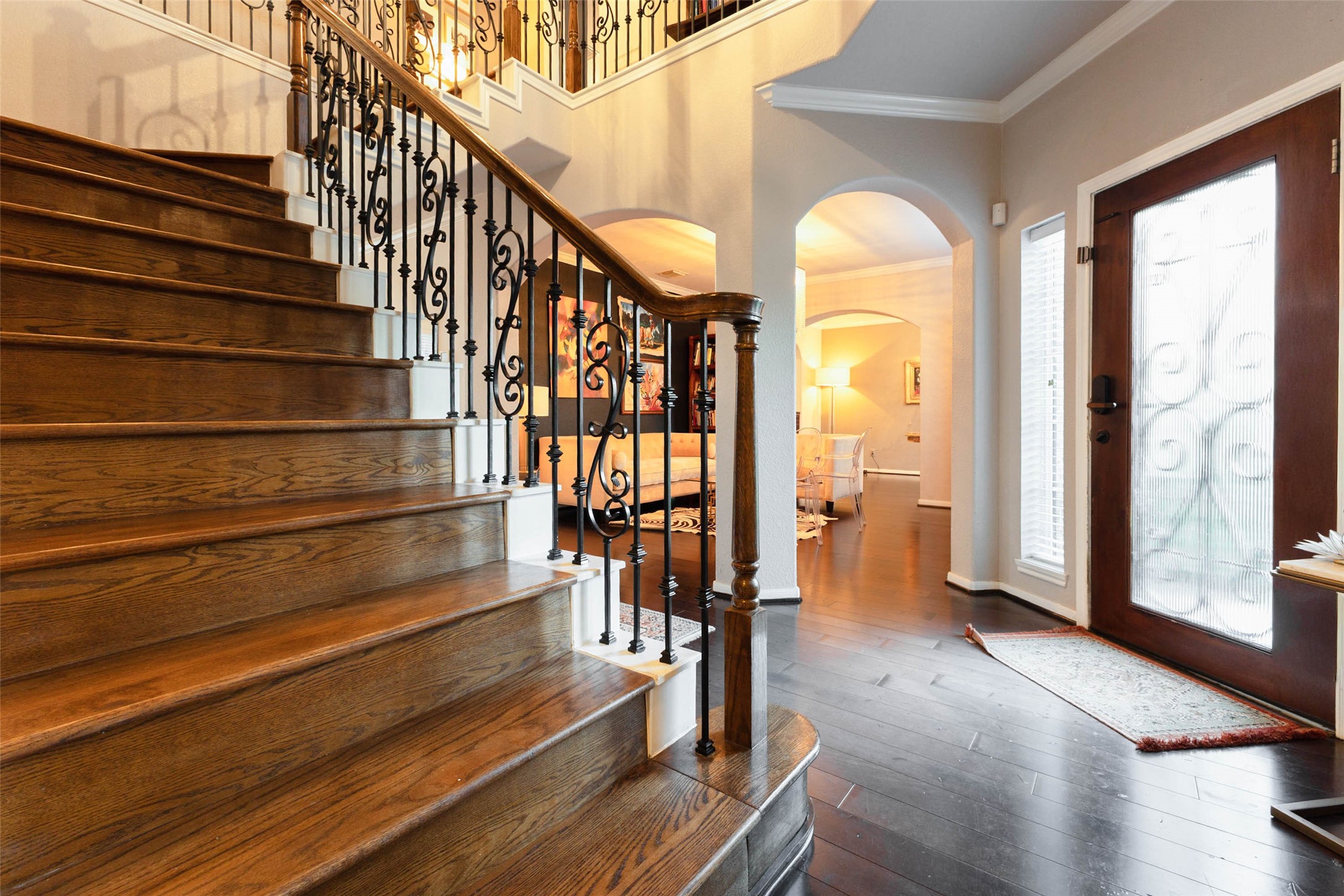 Stately wood steps and decorative iron balusters create a striking focal point beneath the soaring foyer ceiling.