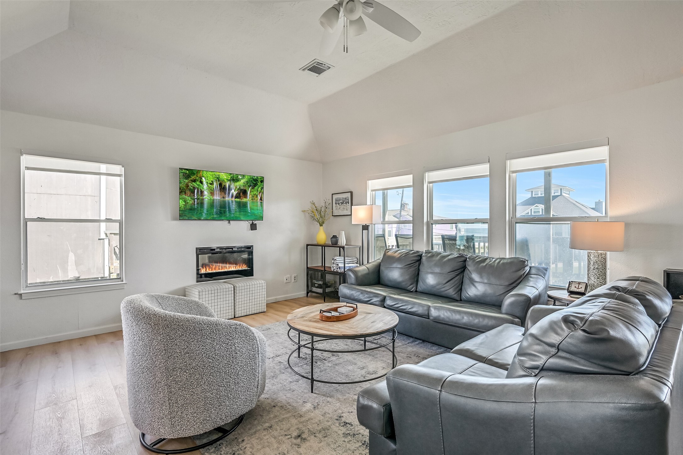 The spacious living room boasts walls of windows that fill the space with natural light, beautiful beach views, and an electric fireplace that adds a cozy touch.