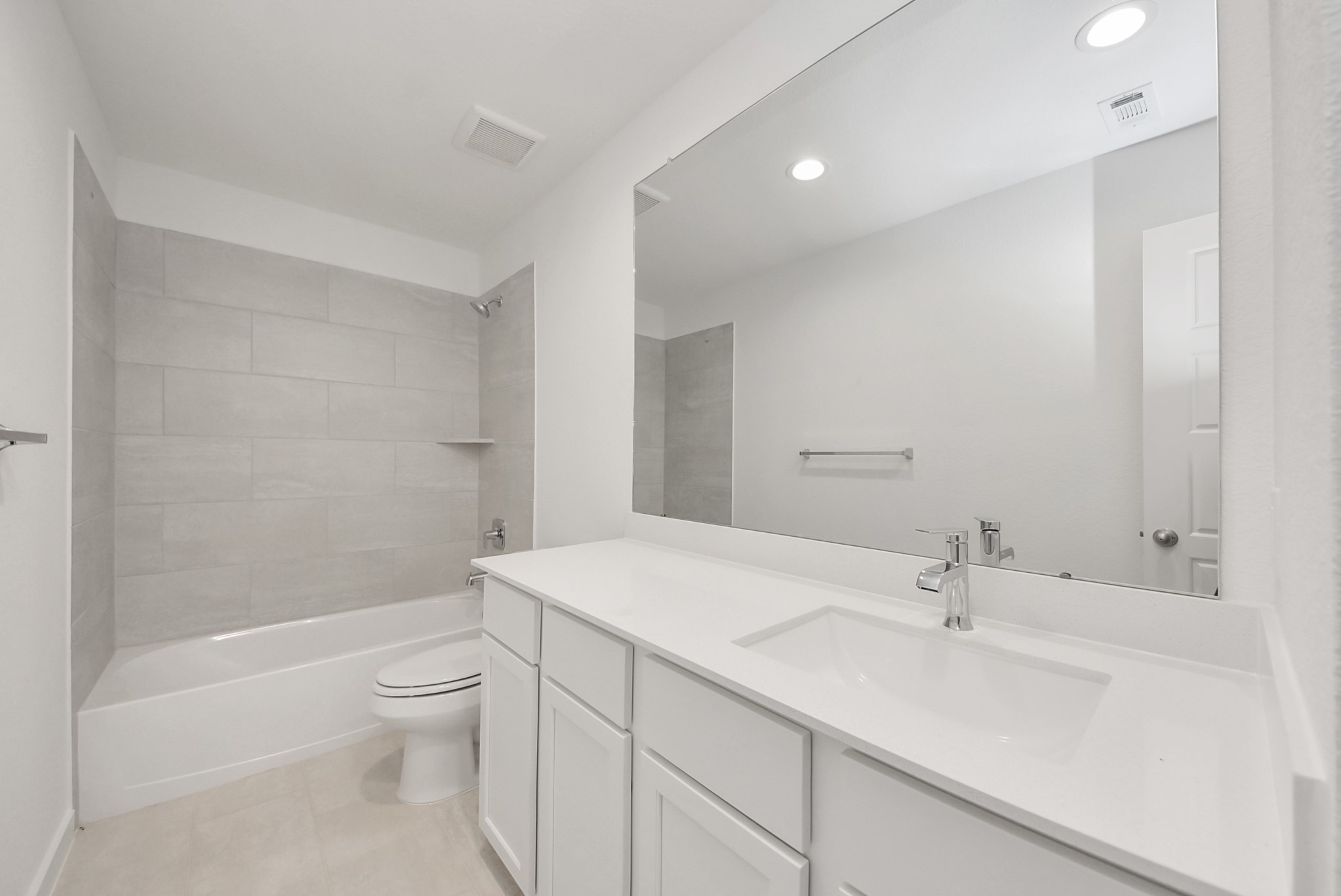 Secondary bath features tile flooring, bath/shower combo with tile surround, light stained wood cabinets, beautiful light countertop.