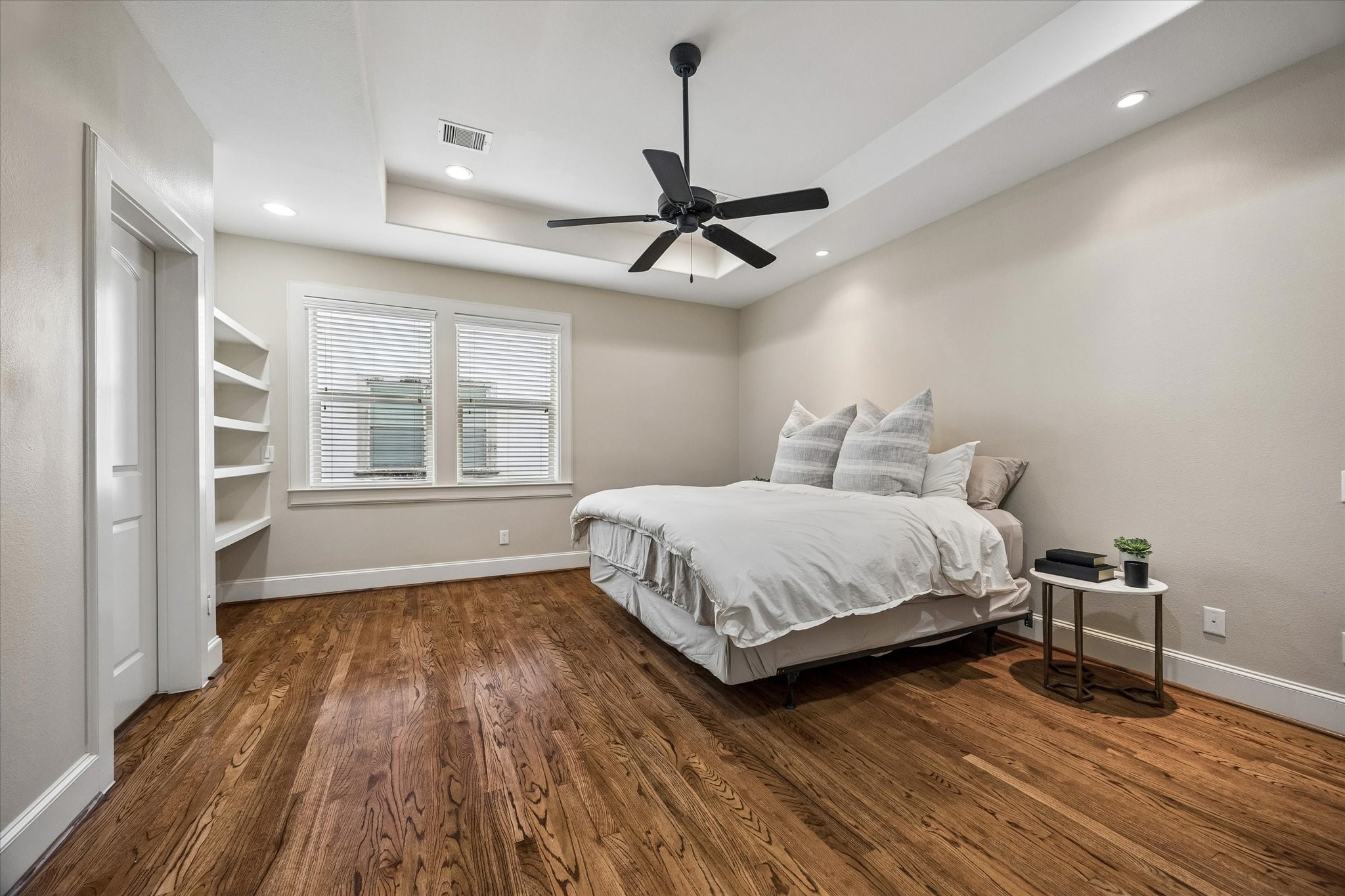 The primary bedroom features built-in shelving, a large window, and lovely recessed ceiling.