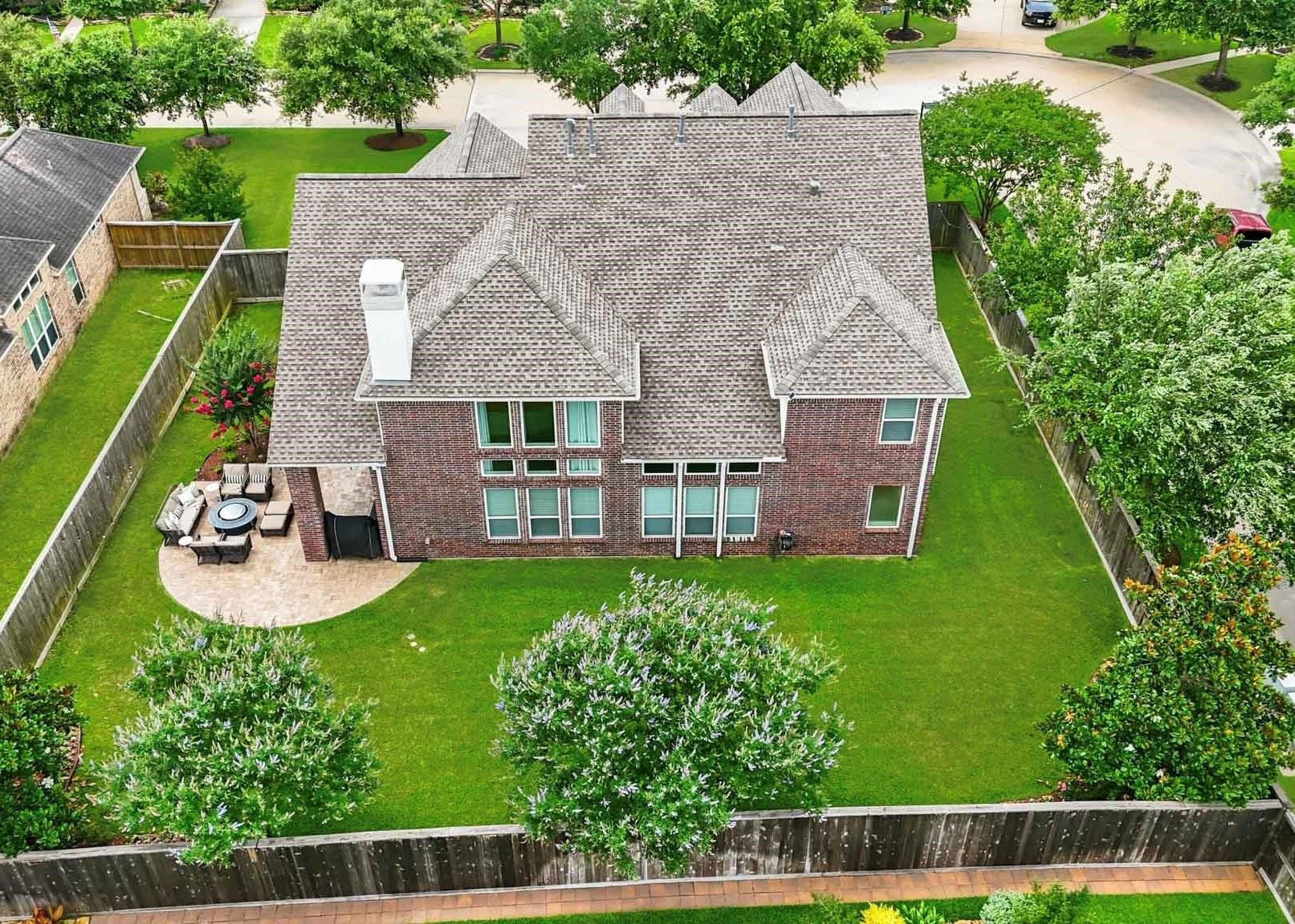 A birds-eye view reveals one of the homes most impressive features: a resort-inspired backyard with lush green space, mature landscaping, and a spacious paver patio ideal for dining, relaxing, and enjoying the outdoors year-round.