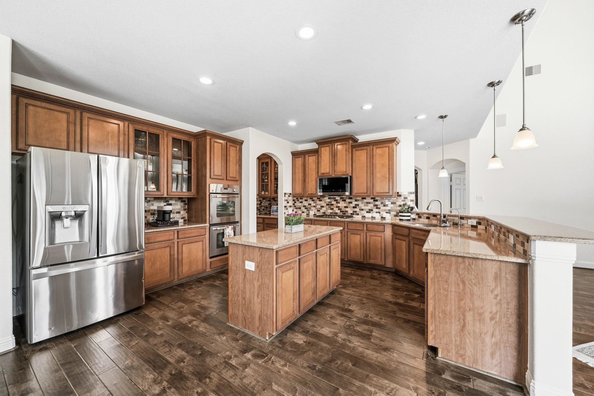 The island litchen provides a suite of premium appliances includes a five-burner gas cooktop, double ovens, microwave and the refrigerator stays with the home, while the coffee bar with granite counters and glass-front display cabinets add both function and sophistication.