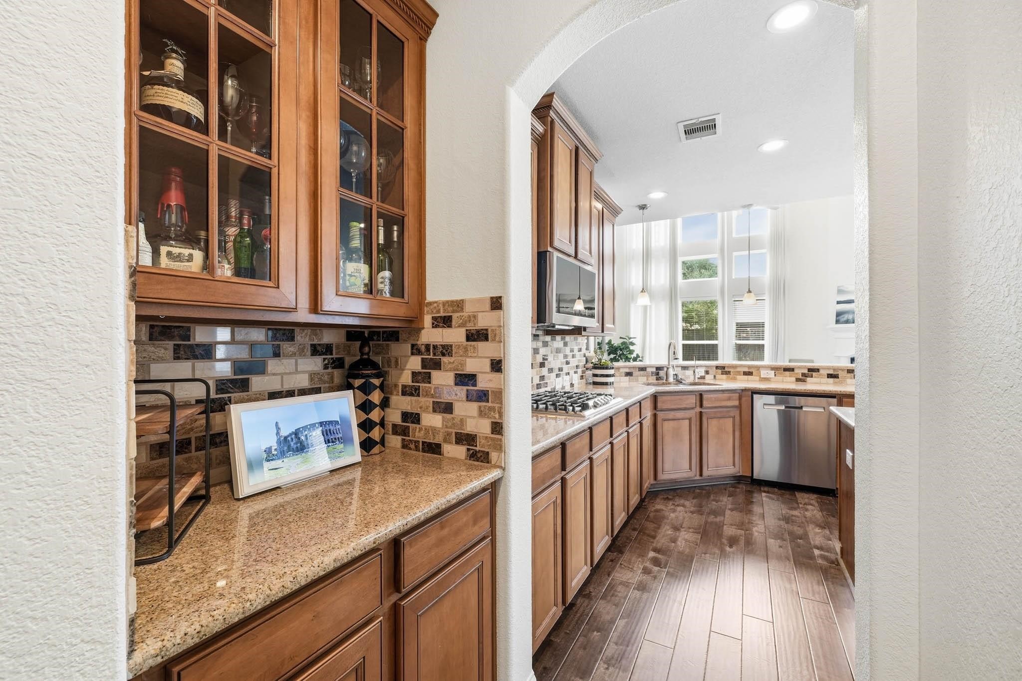 Granite countertops and glass-front cabinetry elevate the butlers pantry, providing a sophisticated setting for entertaining essentials and organized storage.