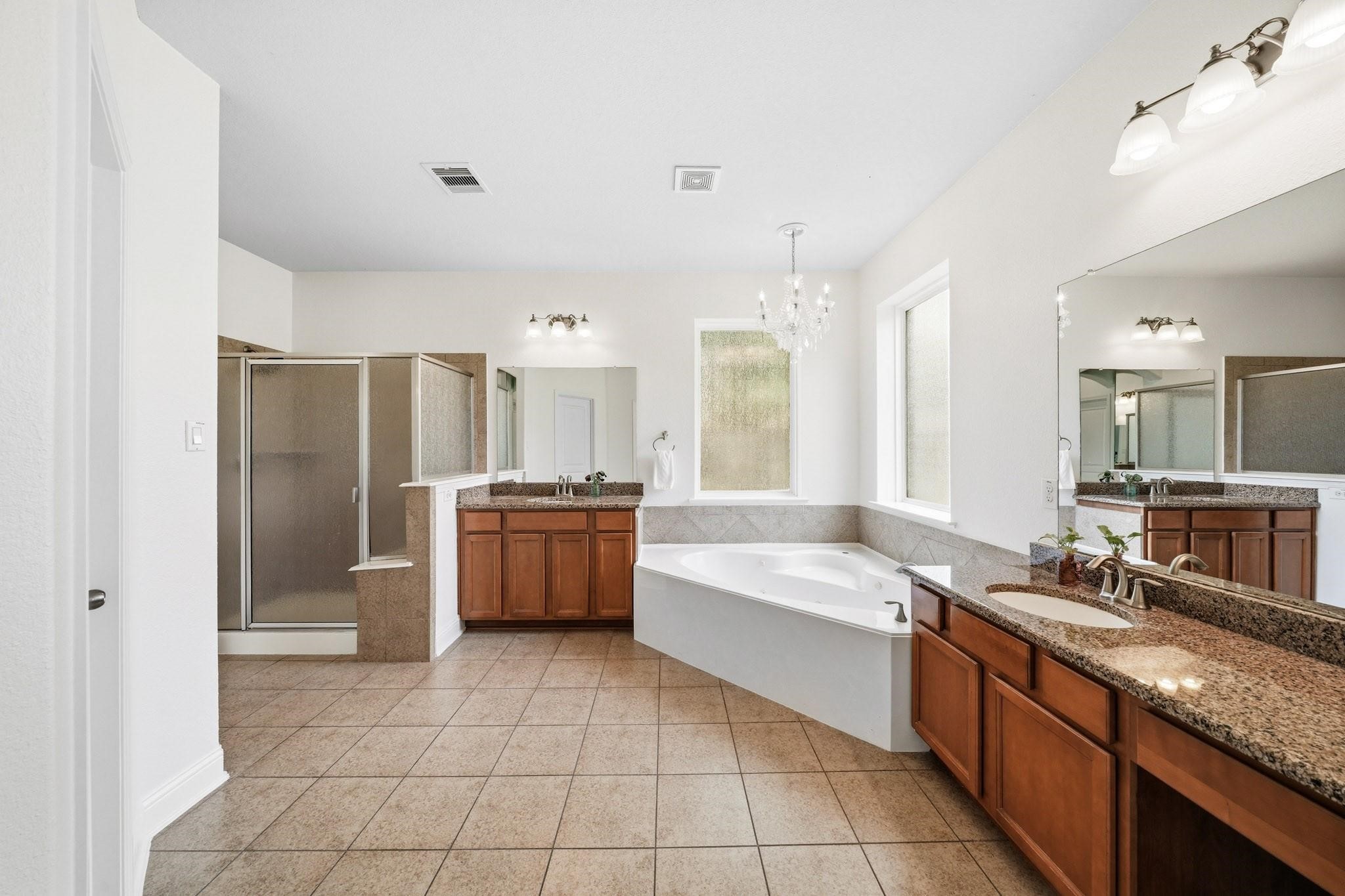 Retreat to a beautifully appointed primary bath where dual sinks, granite counters, a makeup vanity, and elegant tile flooring create a refined space for daily routines.