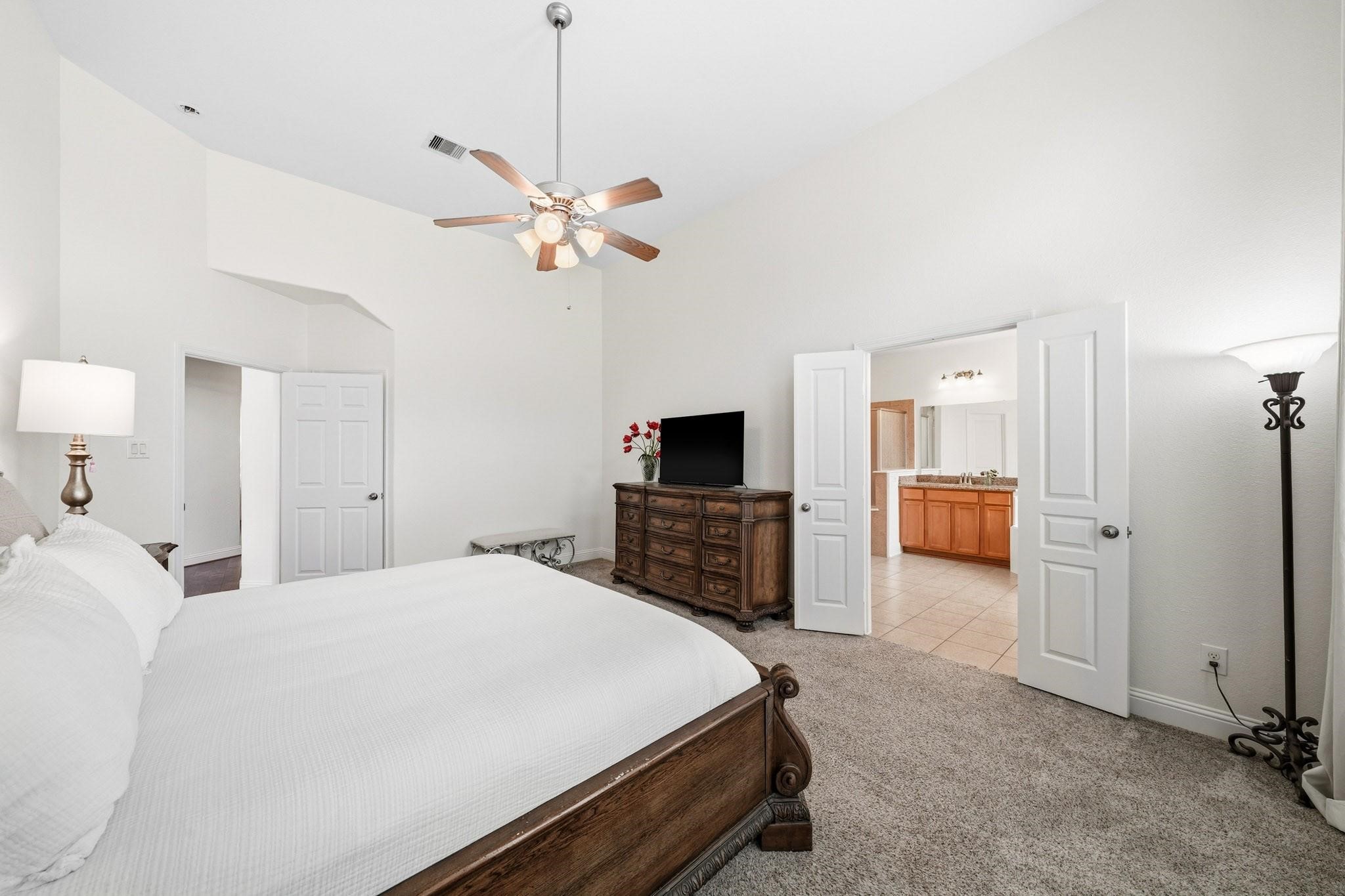 Another view of the primary suite showcased the double-door entry to the primary bath and the ceiling fan with integrated lights create a serene retreat tailored to your comfort at any hour.