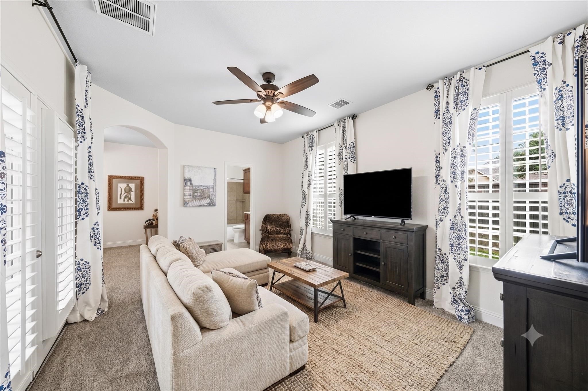 Perfect for guests or multigenerational living, the private secondary suite begins with a charming sitting room filled with natural light, plantation shutters, elegant drapes, and direct access to the front porch through a 6-foot patio door. This photo has been virtually staged.