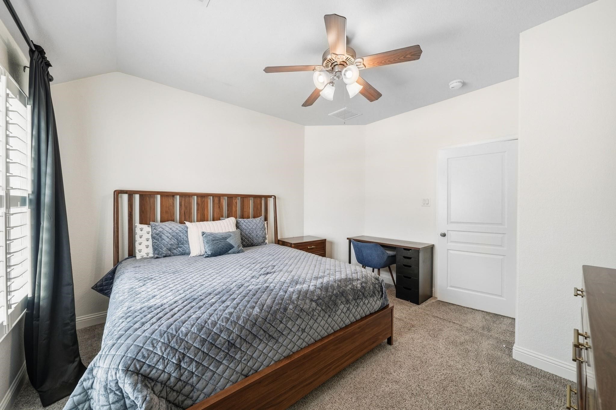 Soft natural light filters through elegant plantation shutters, while a ceiling fan with integrated light enhances the inviting atmosphere of this peaceful third-bedroom retreat.