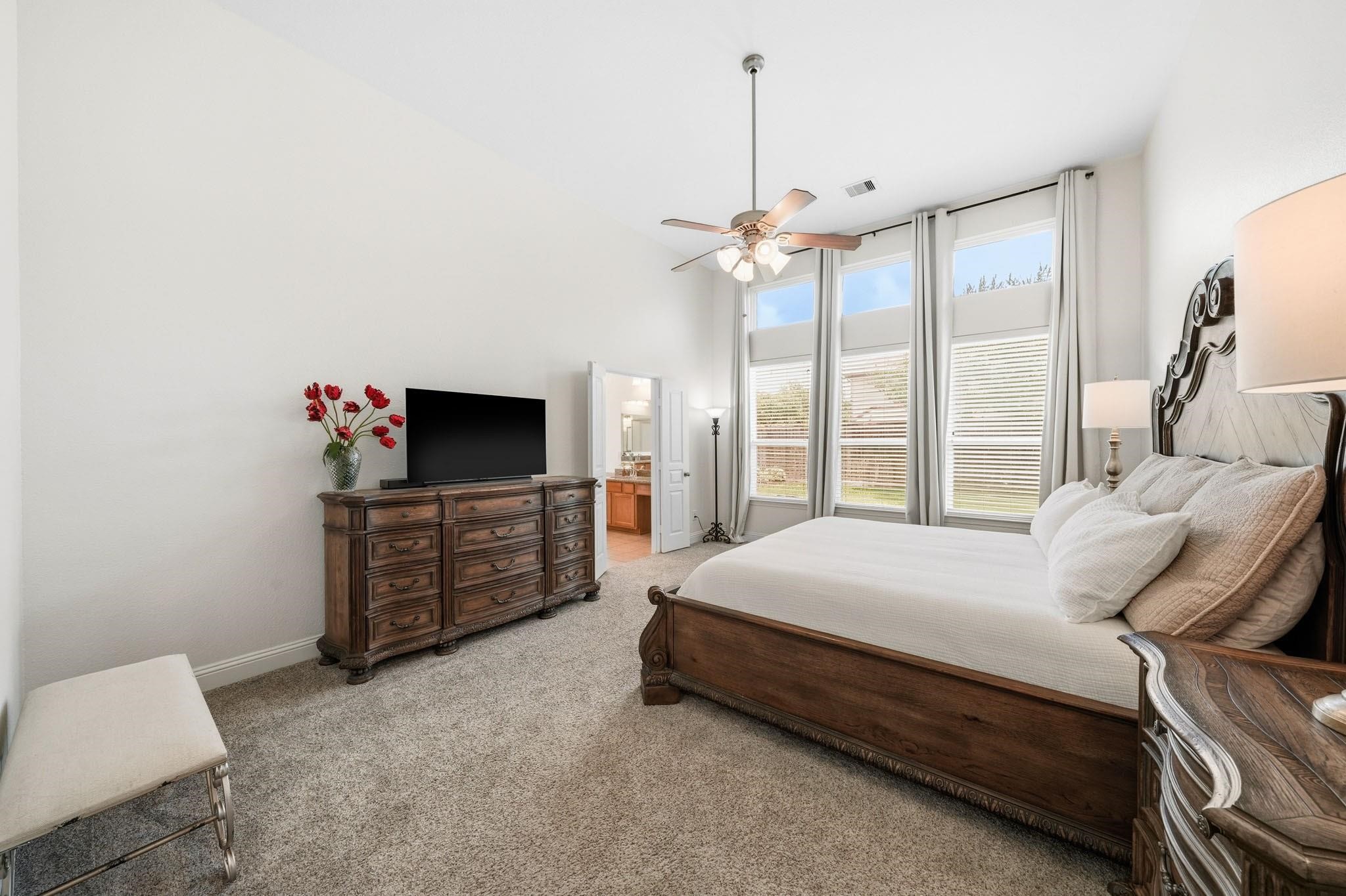 Windows with elegant drapes stretch toward the ceiling, filling this primary bedroom space with sunlight and showcasing beautiful outdoor views.