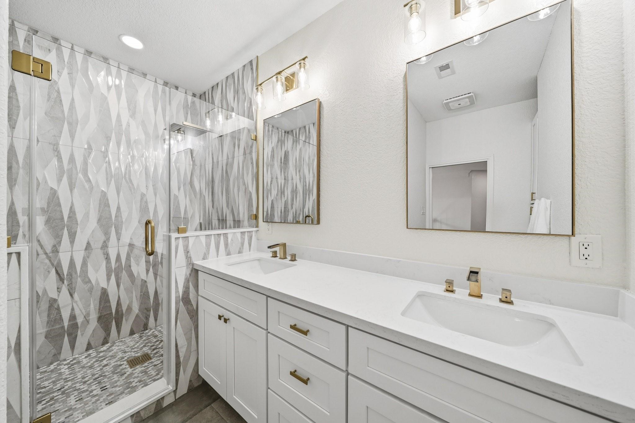 The fourth bath is a true showpiece, remoldeled featuring oversized 12x24 tile floors, dual sink Quartz-topped vanities, designer gold fixtures and mirrors, and a spectacular frameless shower wrapped in floor-to-ceiling tile with both a rain head and separate spray wand.