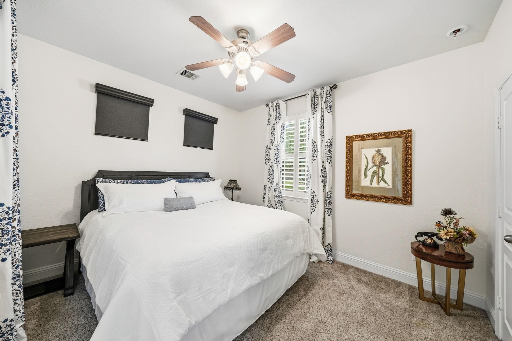 The bedroom within the suite has windows with blinds, drapes and a ceiling fan with integrated light, creating a charming retreat for guests or multigenerational living.
