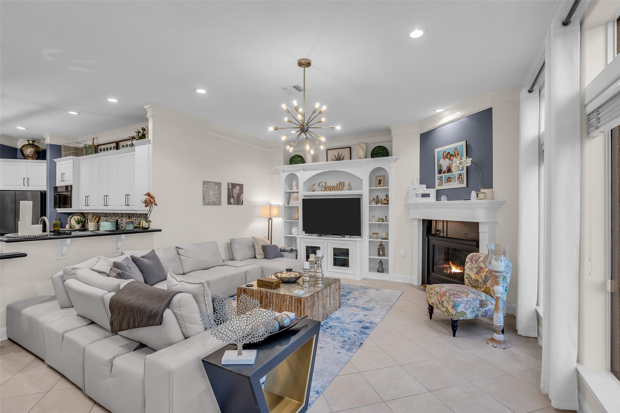Spacious living room with a cozy fireplace, elegant built-in shelving, and a modern light fixture. The open layout flows seamlessly into a stylish kitchen, perfect for entertaining.