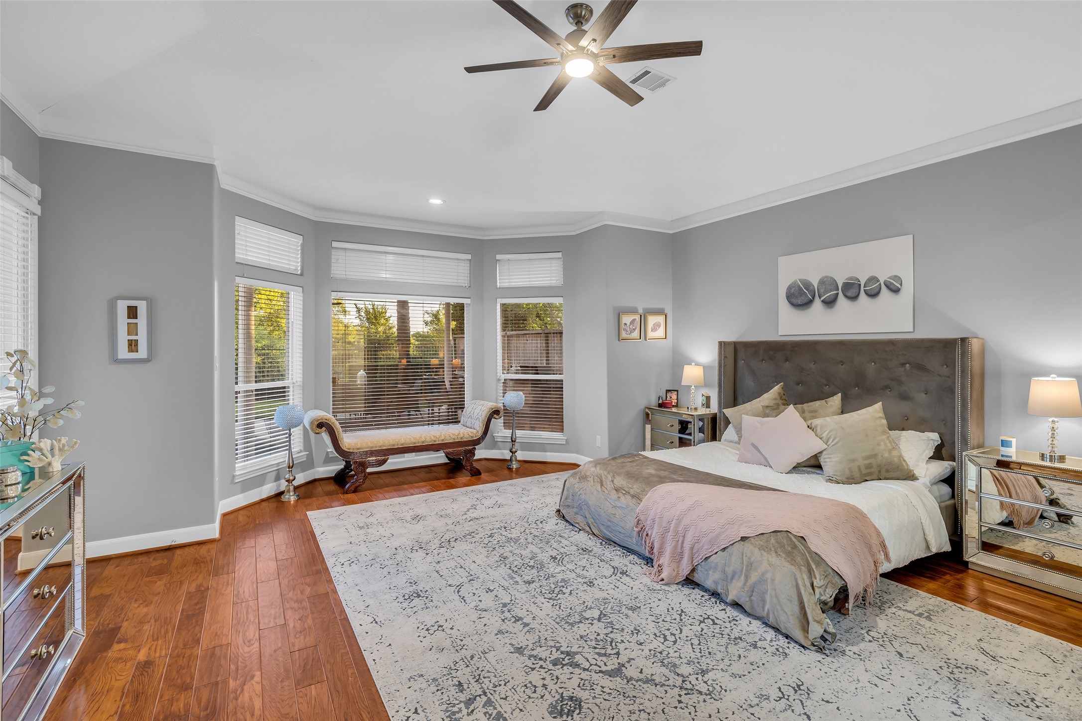 Spacious primary bedroom featuring elegant wood floors, a cozy seating area by large bay windows, and a stylish ceiling fan, creating a serene retreat.