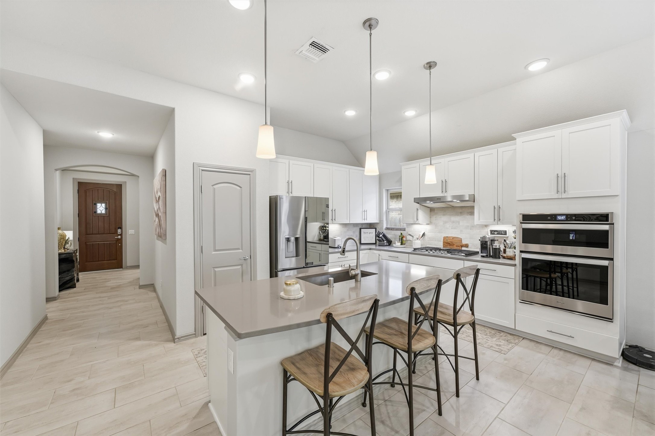 Beautifully appointed kitchen featuring white cabinetry, stainless steel appliances, a large center island, and stylish pendant lighting.