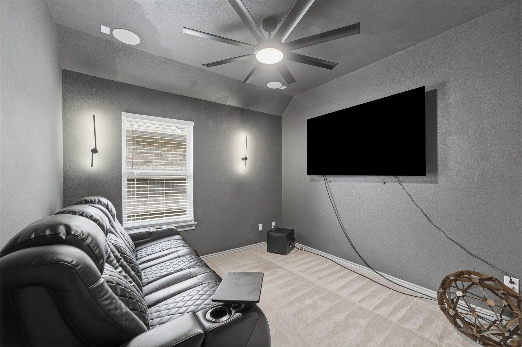 Dedicated media room featuring a large wall-mounted TV, comfortable theater seating, modern lighting, and ceiling fan.