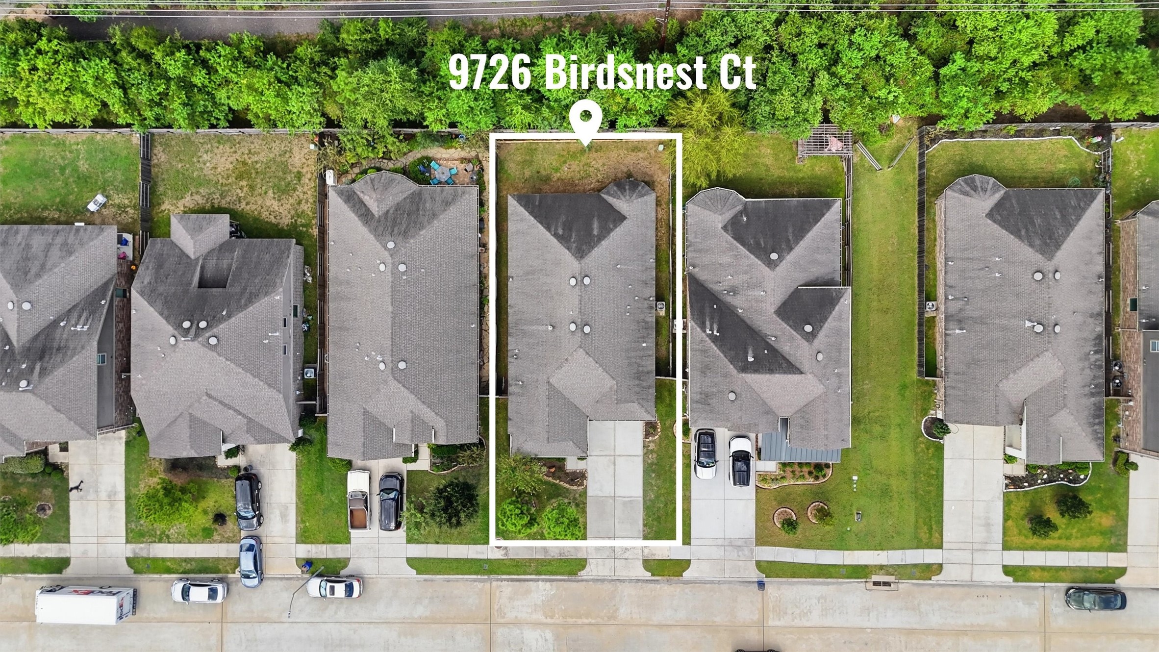 Overhead aerial view highlighting the home's lot, driveway, and backyard, with a wooded greenbelt beyond the rear fence.