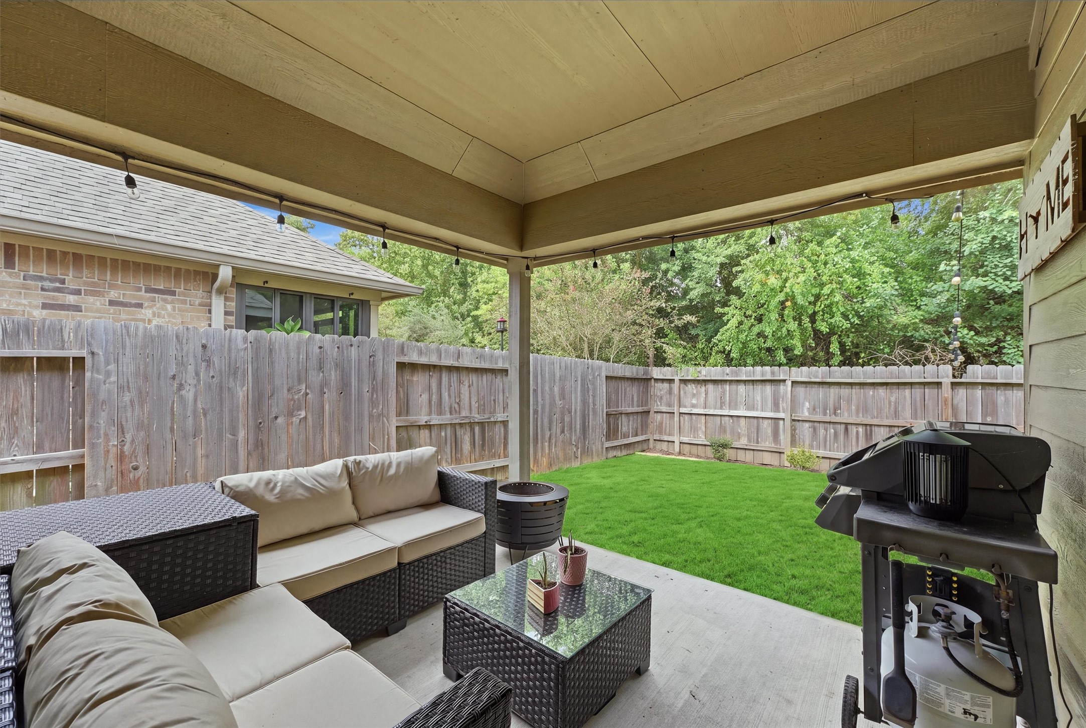 Inviting covered patio with outdoor seating, string lighting, and grilling area overlooking the private, fenced backyard.