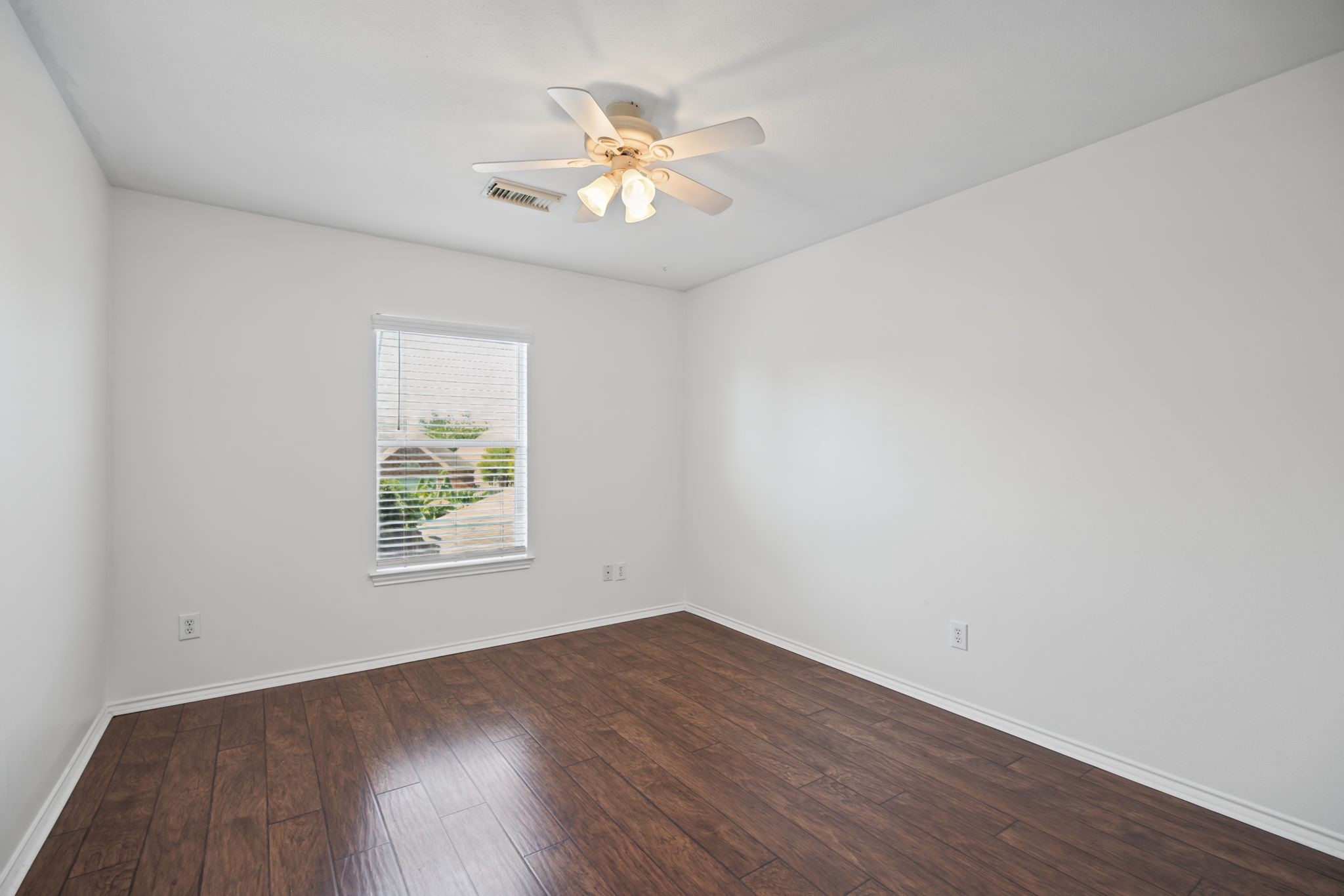 Continue to another bedroom, where dark-toned flooring, natural light, and a ceiling fan create a warm, restful setting.