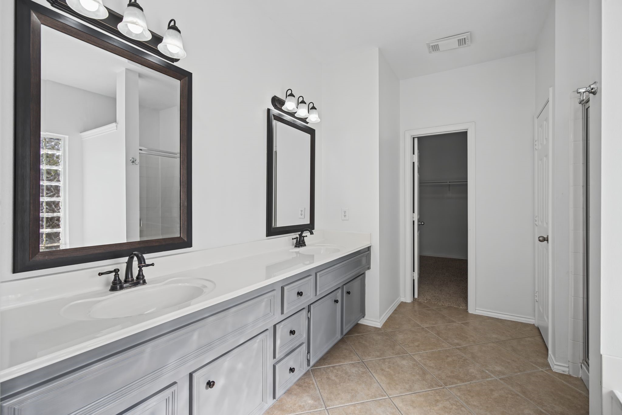 The primary bathroom offers an extended double-sink vanity, framed mirrors, and coordinating lighting for a balanced, refined presentation.