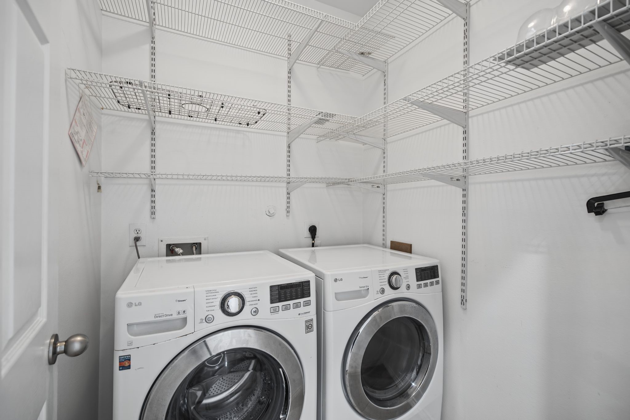 The laundry area brings everyday convenience into focus, with shelving above and around the washer and dryer.