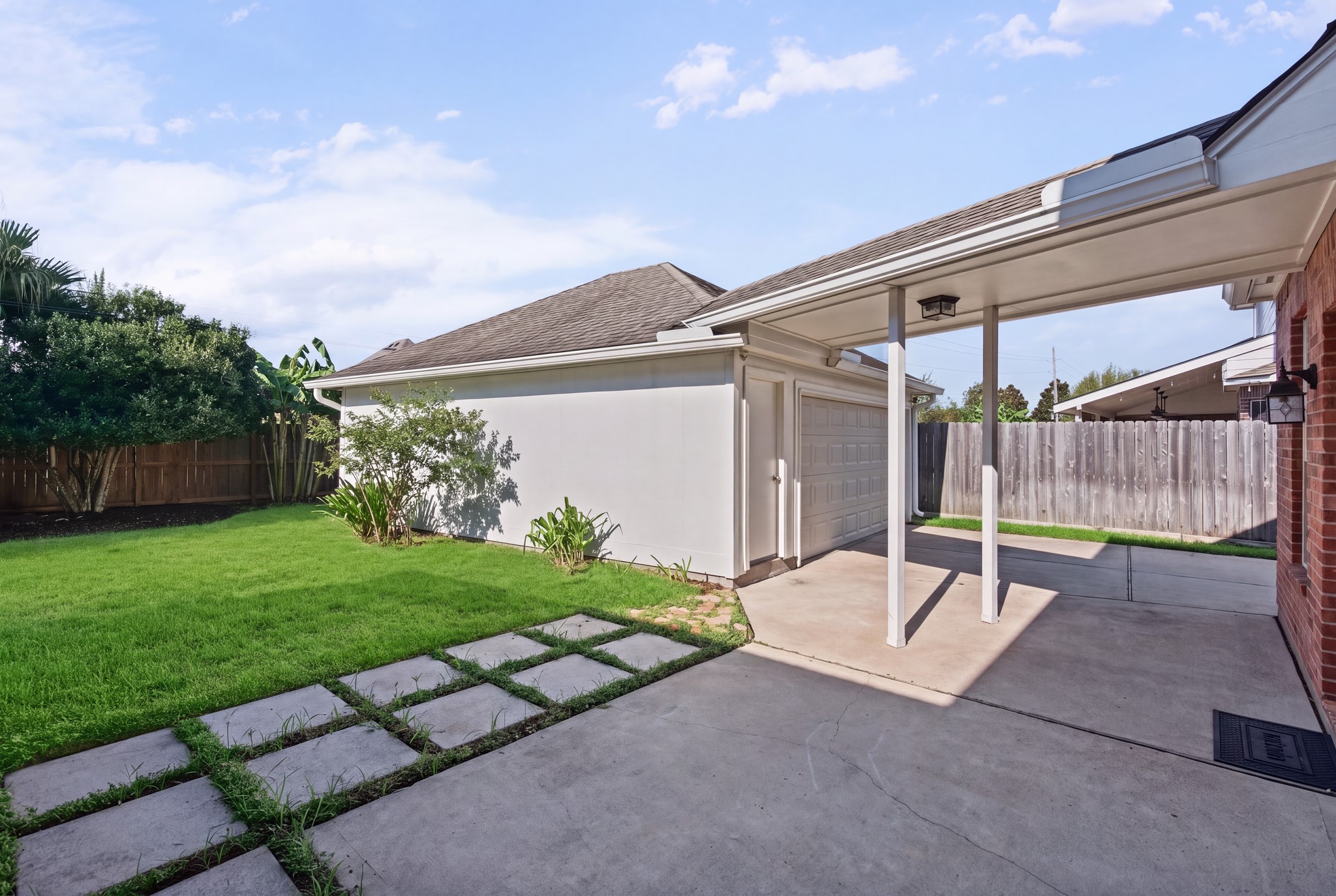 Step outdoors to a paved patio and covered passage linking the house and garage, with stepping stones extending into the lawn. Sellers installed a smart irrigation device (rachio 3) for sprinkler controllers.