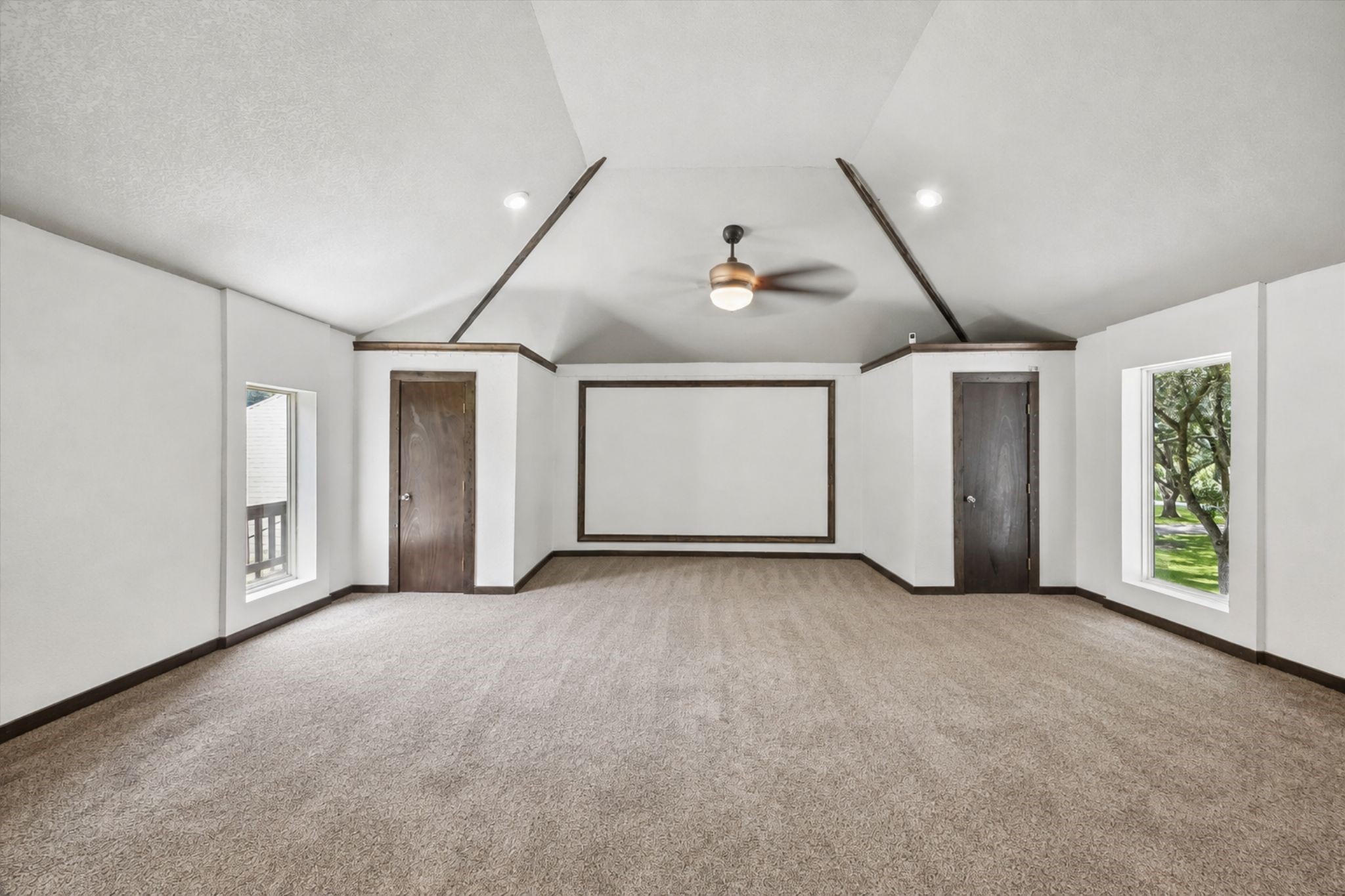 OVERSIZED GAME ROOM FEATURES A VAULTED CEILING, CARPET FLOORING, MULTIPLE WINDOWS, AND A LARGE BUILT-IN SCREEN AREA.