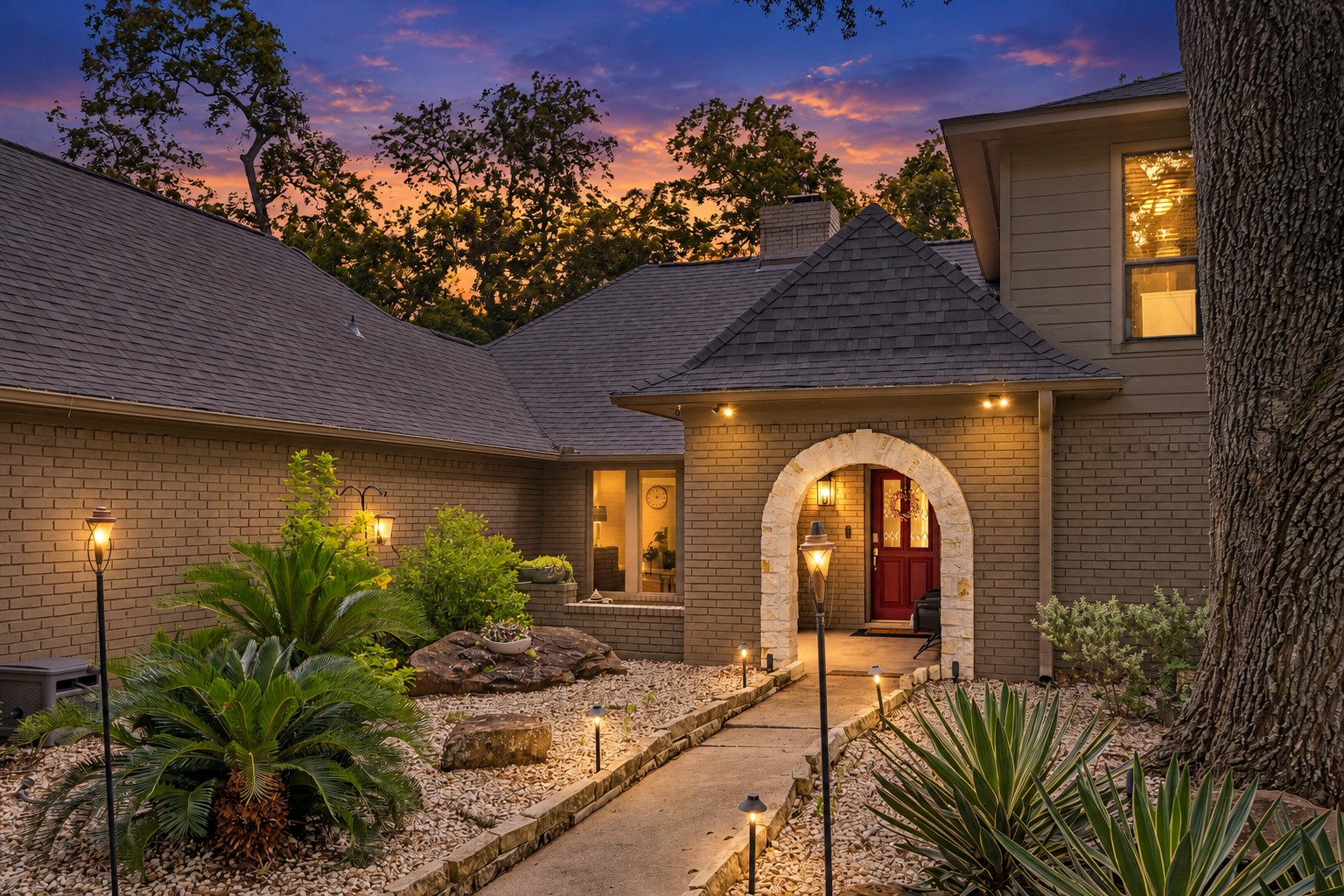 COVERED ARCHED ENTRY IS COMPLEMENTED BY MATURE LANDSCAPING, STONE ACCENTS, AND A LANDSCAPED COURTYARD-STYLE APPROACH.