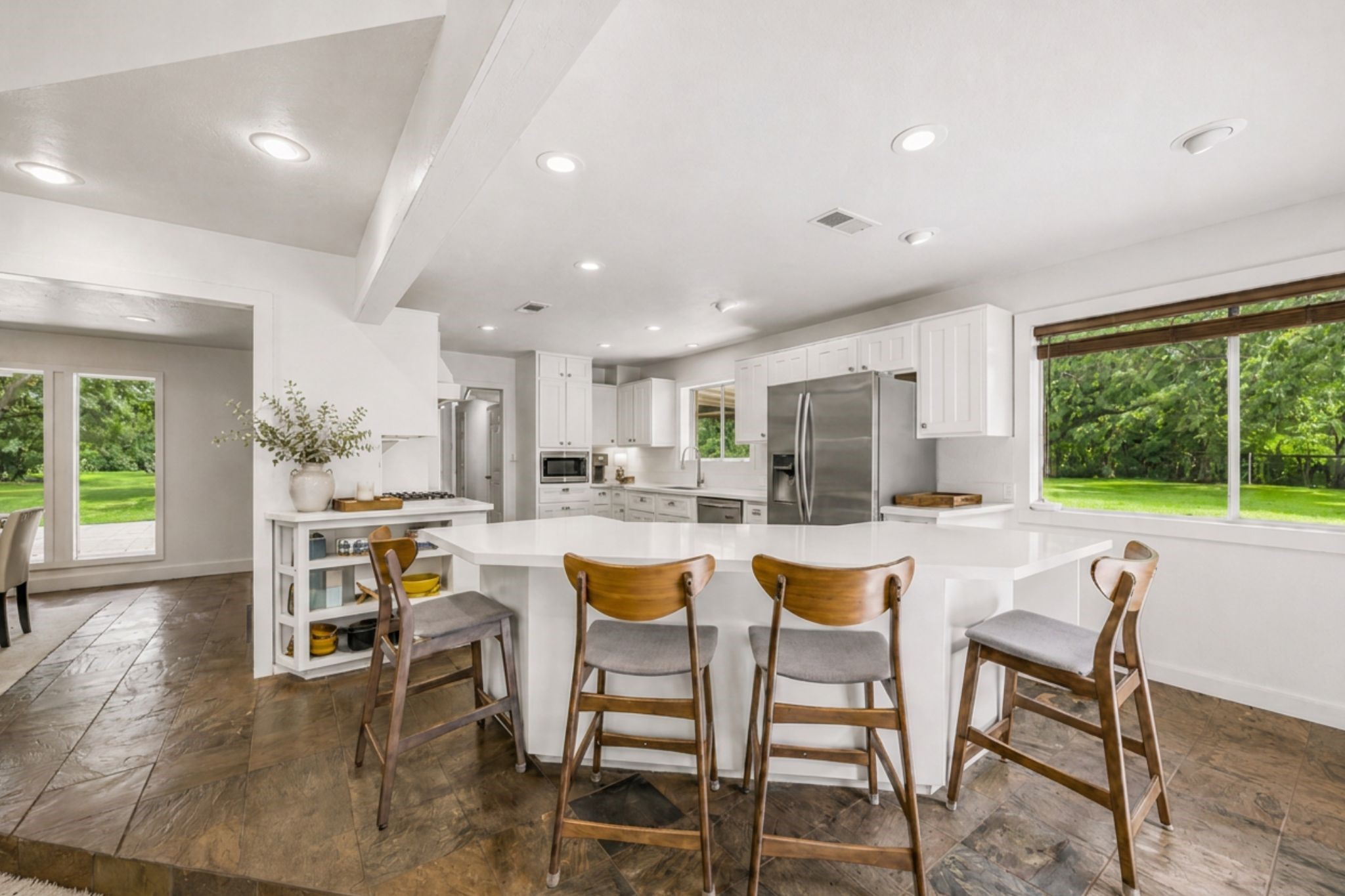 LARGE KITCHEN OFFERS A GENEROUS BREAKFAST BAR, ABUNDANT CABINET AND COUNTER SPACE, STAINLESS STEEL APPLIANCES, AND LARGE WINDOWS OVERLOOKING THE PROPERTY.