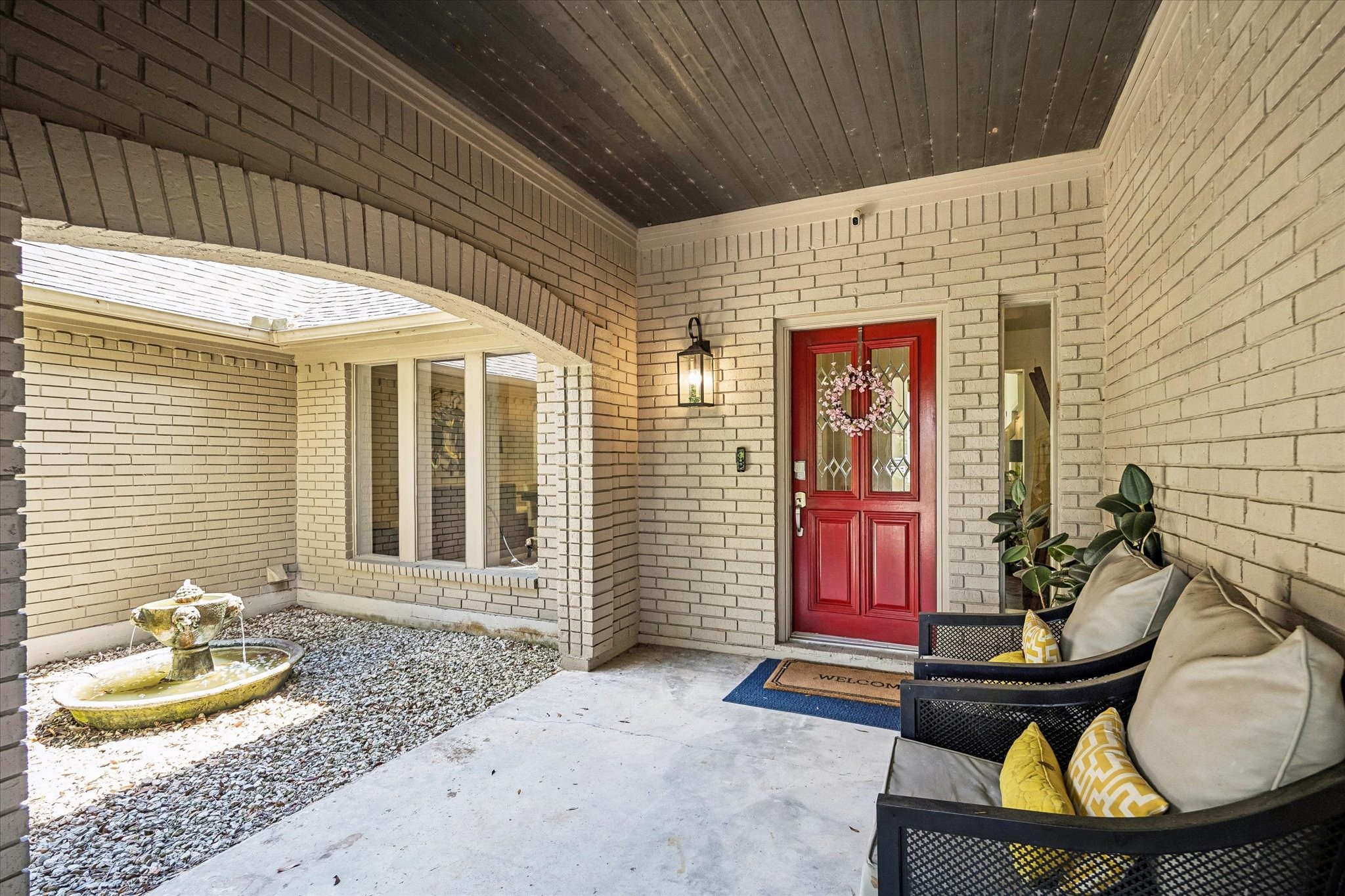 COVERED FRONT ENTRY FEATURES BRICK SURROUND, AN ARCHED OPENING, AND A SHELTERED COURTYARD AREA LEADING TO THE MAIN DOOR.