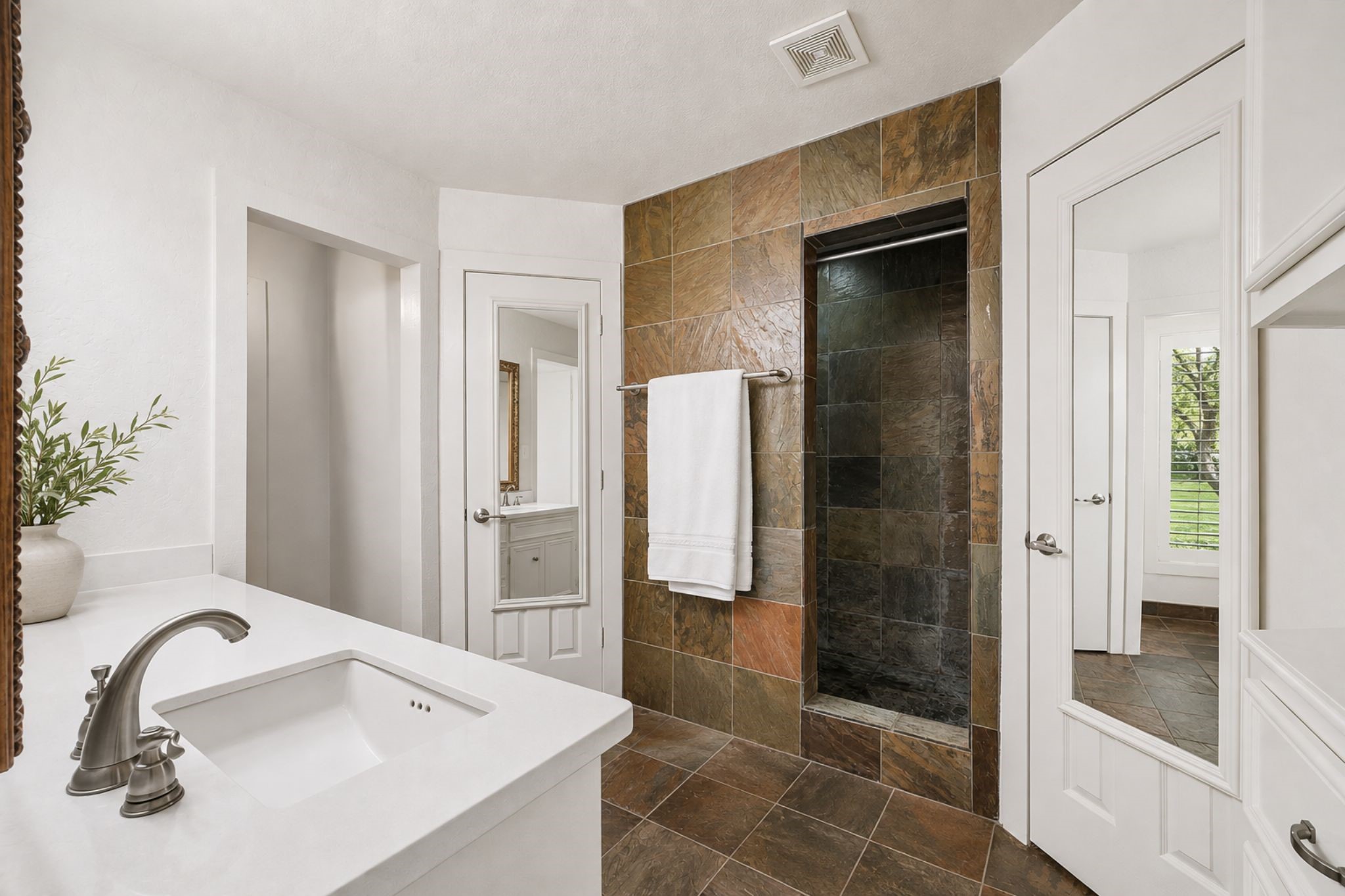 BATHROOM FEATURES AN EXPANSIVE VANITY, WALK-IN TILED SHOWER, ABUNDANT BUILT-IN STORAGE, AND COORDINATING TILE FLOORING.