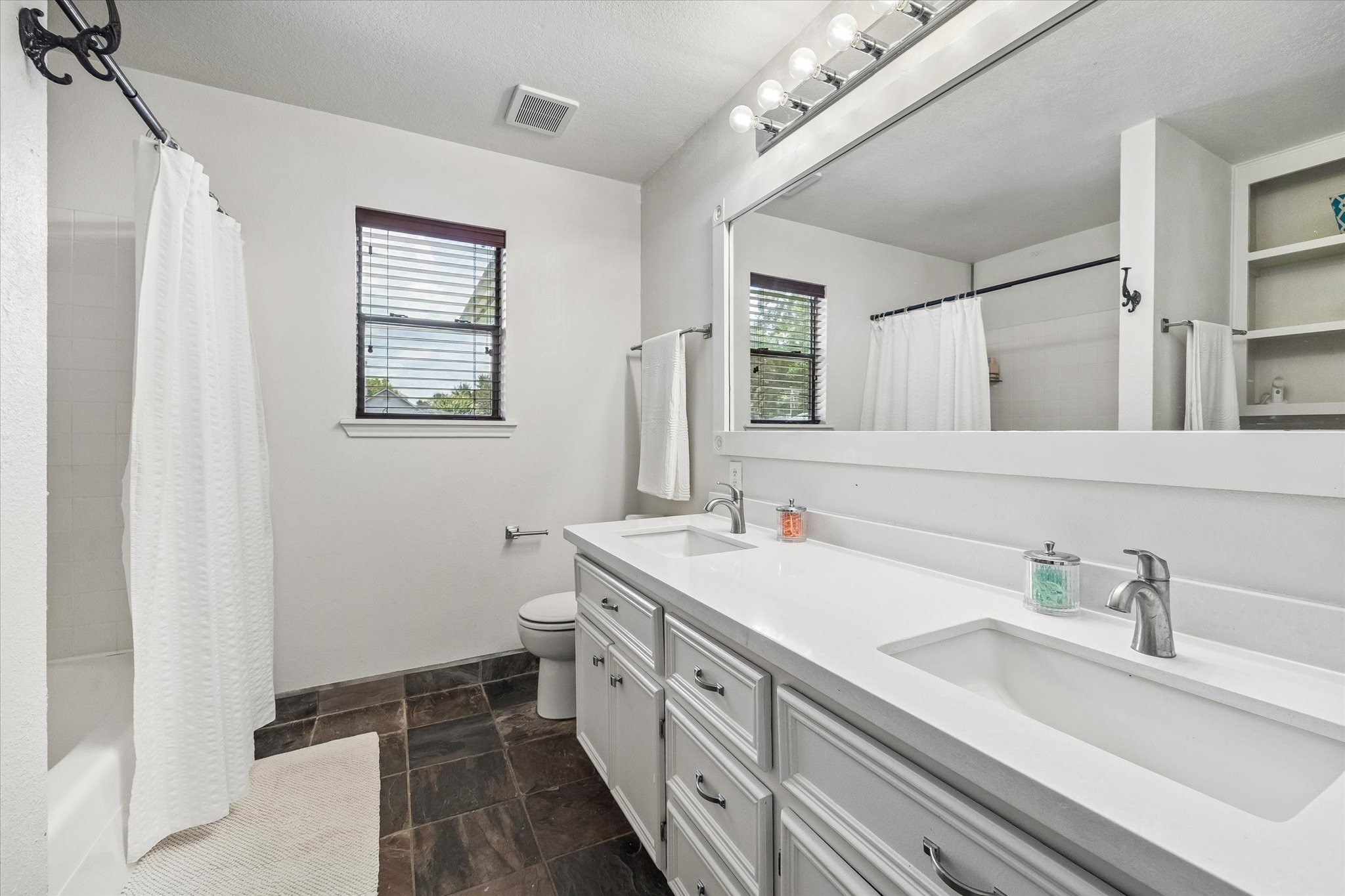 SECONDARY BATHROOM FEATURES A LONG DUAL-SINK VANITY, OVERSIZED MIRROR, TUB/SHOWER COMBINATION, AND TILE FLOORING.