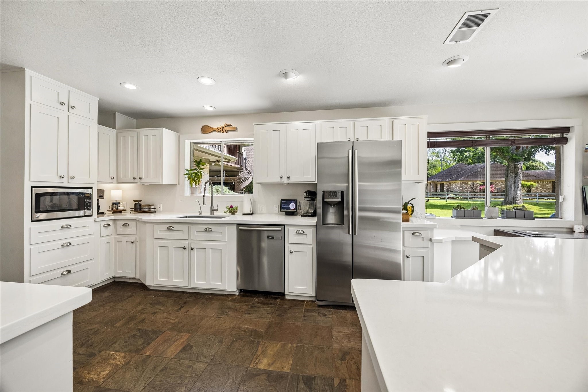 SPACIOUS KITCHEN OFFERS EXTENSIVE WHITE CABINETRY, GENEROUS COUNTER SPACE, STAINLESS STEEL APPLIANCES, AND LARGE WINDOWS OVERLOOKING THE GROUNDS.