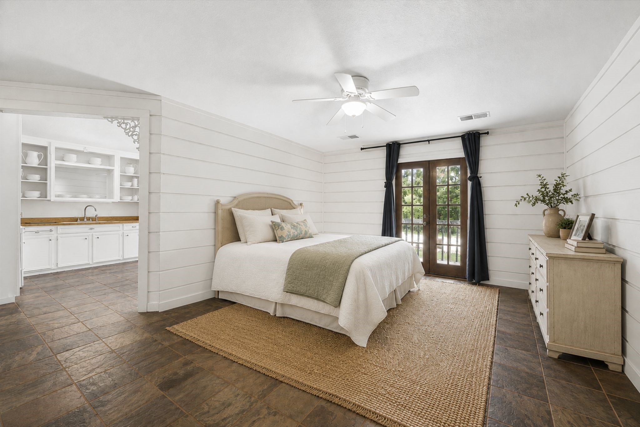GUEST HOUSE BEDROOM FEATURES SHIPLAP-STYLE WALL DETAILING, TILE FLOORING, CEILING FAN, AND FRENCH DOORS PROVIDING EXTERIOR ACCESS.