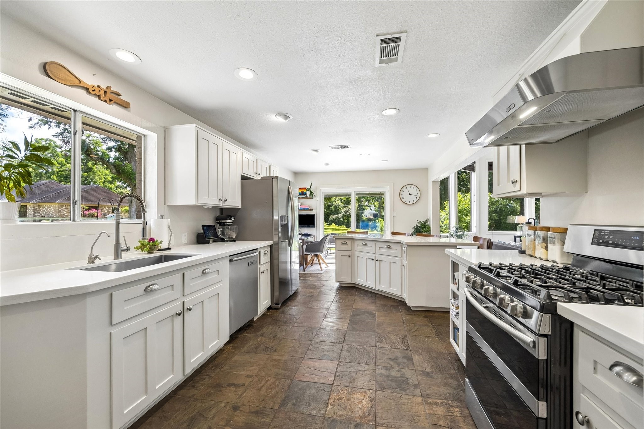 BRIGHT KITCHEN FEATURES ABUNDANT CABINETRY, EXTENSIVE COUNTER SPACE, STAINLESS STEEL APPLIANCES, A GAS RANGE, AND MULTIPLE WINDOWS FOR NATURAL LIGHT.