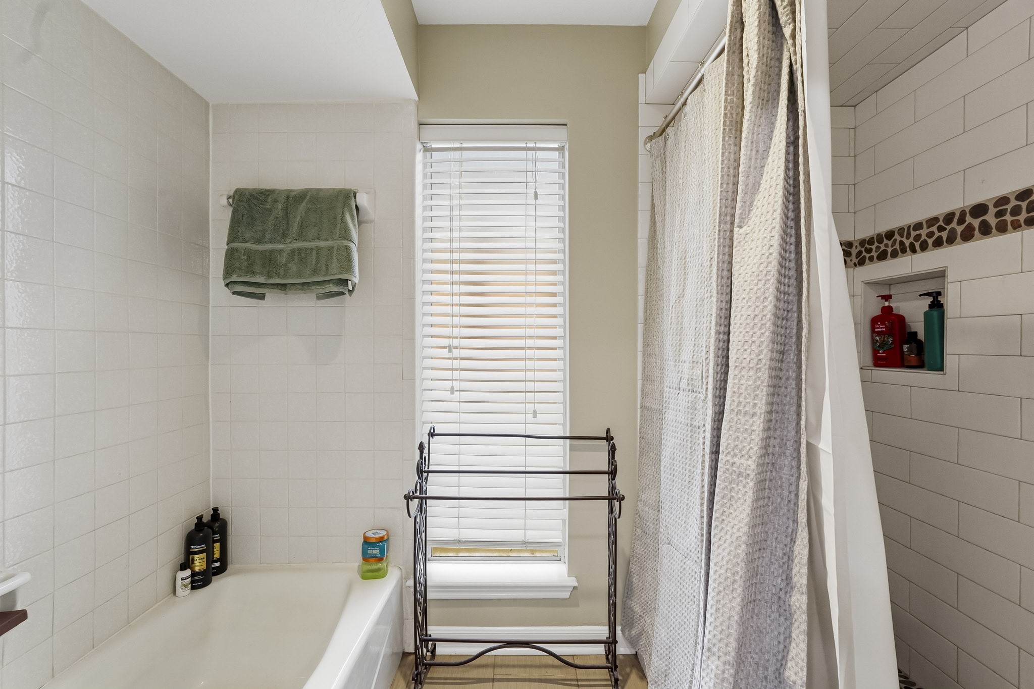 Bright bathroom with a cozy tub and shower combo, featuring stylish tile accents and ample natural light through large windows.