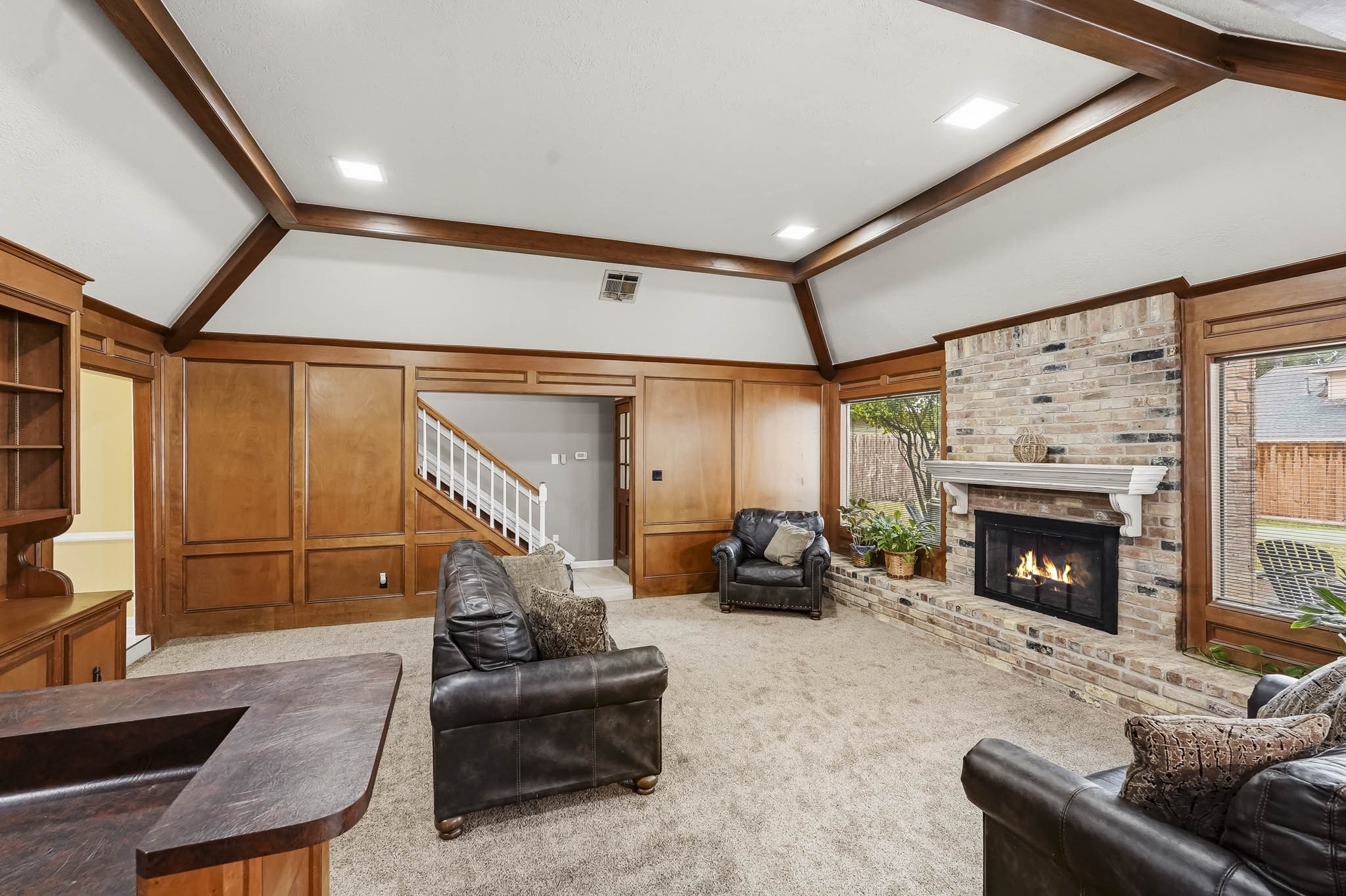 Spacious living room featuring rich wooden paneling and beams, a cozy brick fireplace, and plush carpeting, creating a warm and inviting atmosphere.
