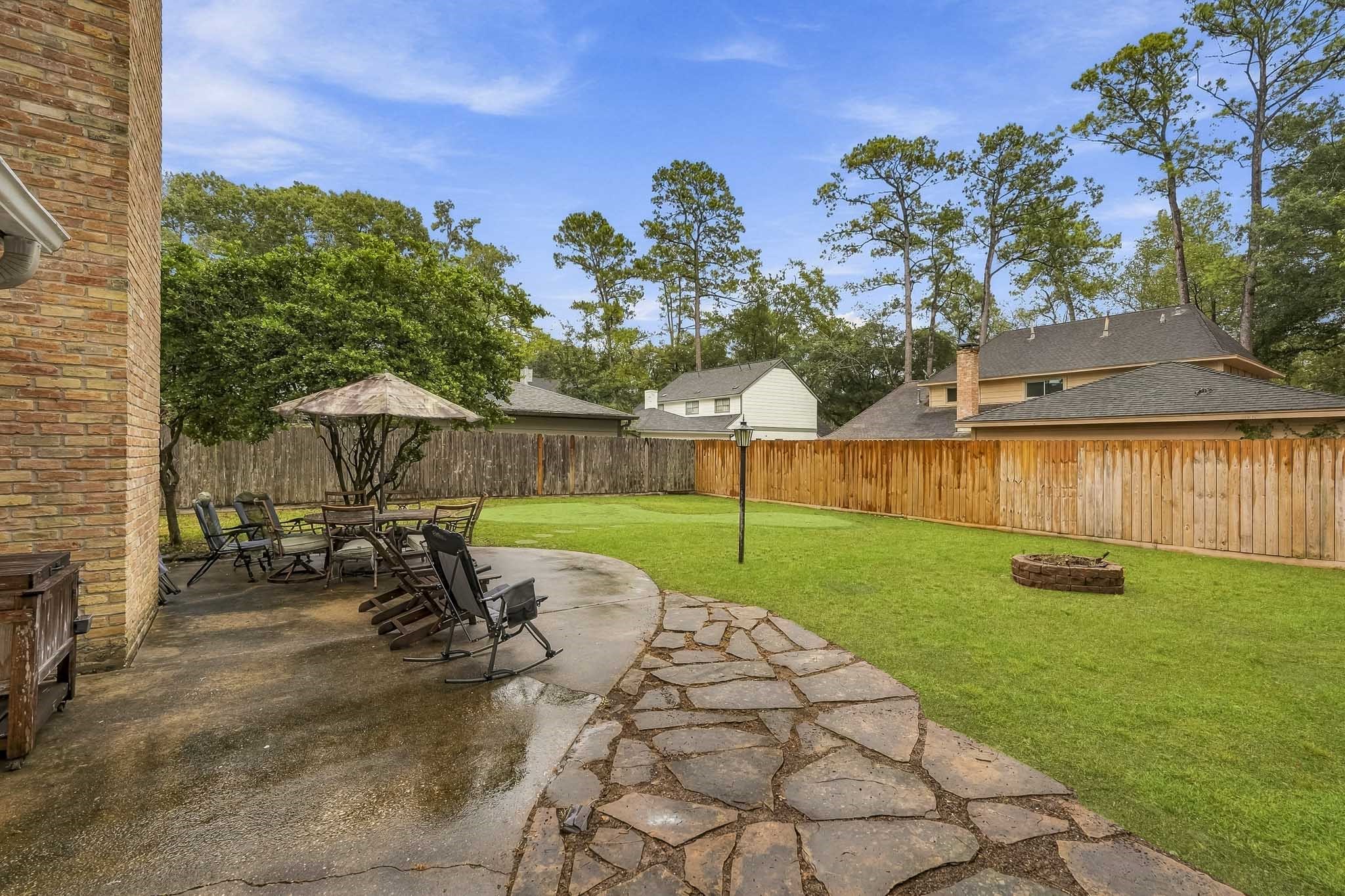 Spacious backyard featuring a large patio with seating area, perfect for outdoor entertaining, surrounded by lush greenery and a cozy fire pit for evening relaxation.